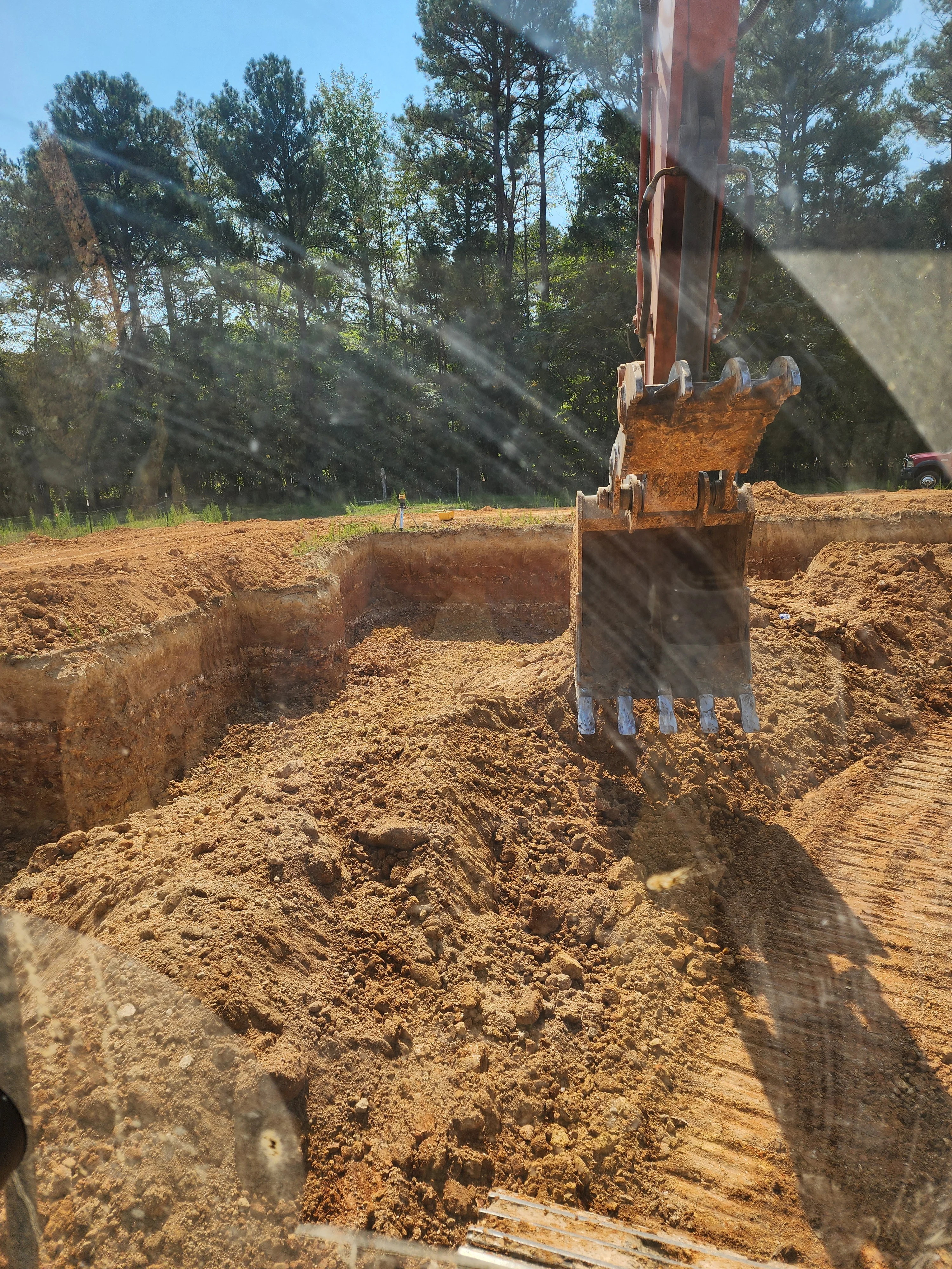 Excavator bucket removing soil from deep foundation trench on wooded property