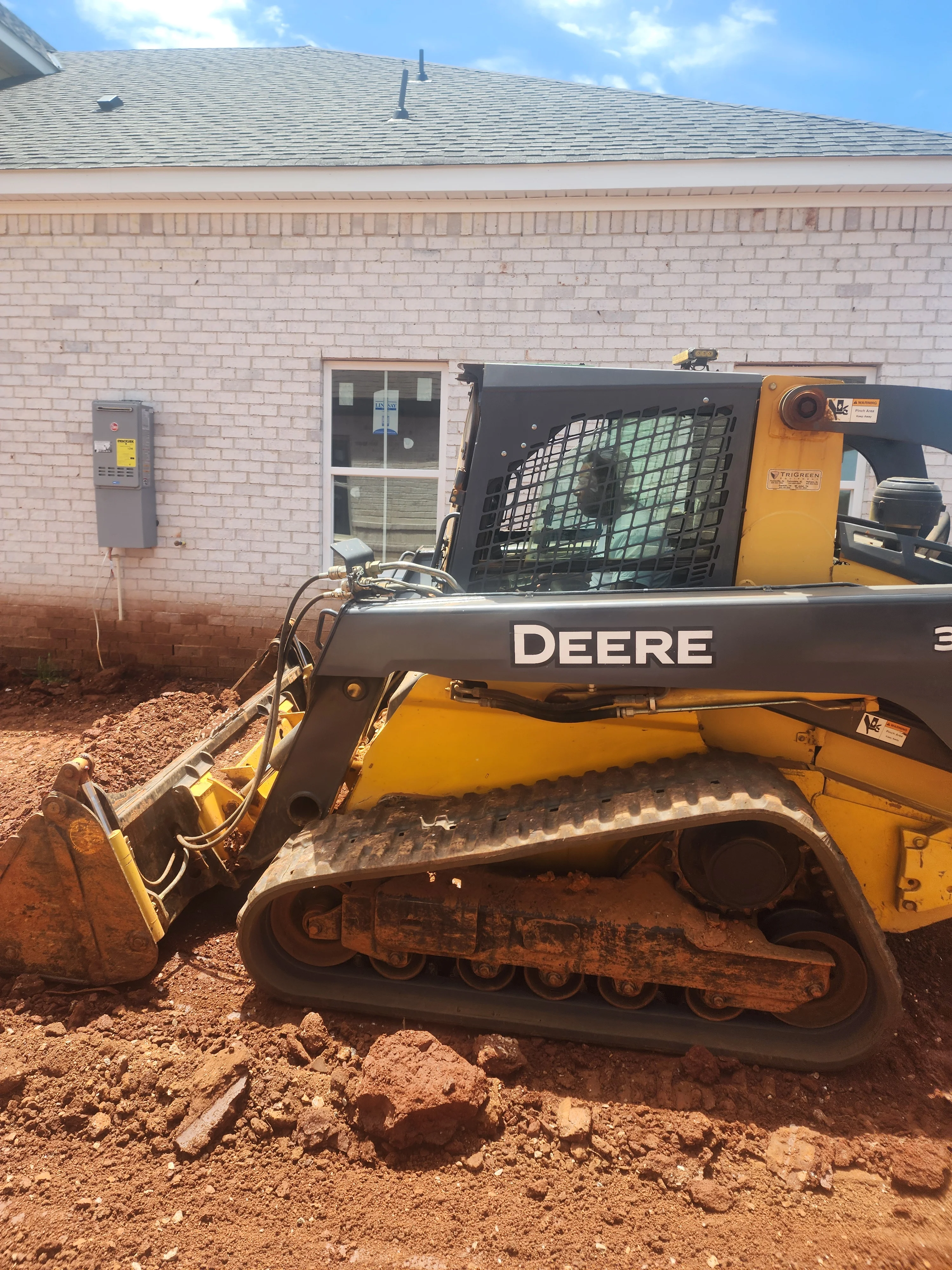 Yellow Deere skid steer loader grading dirt at residential brick home site