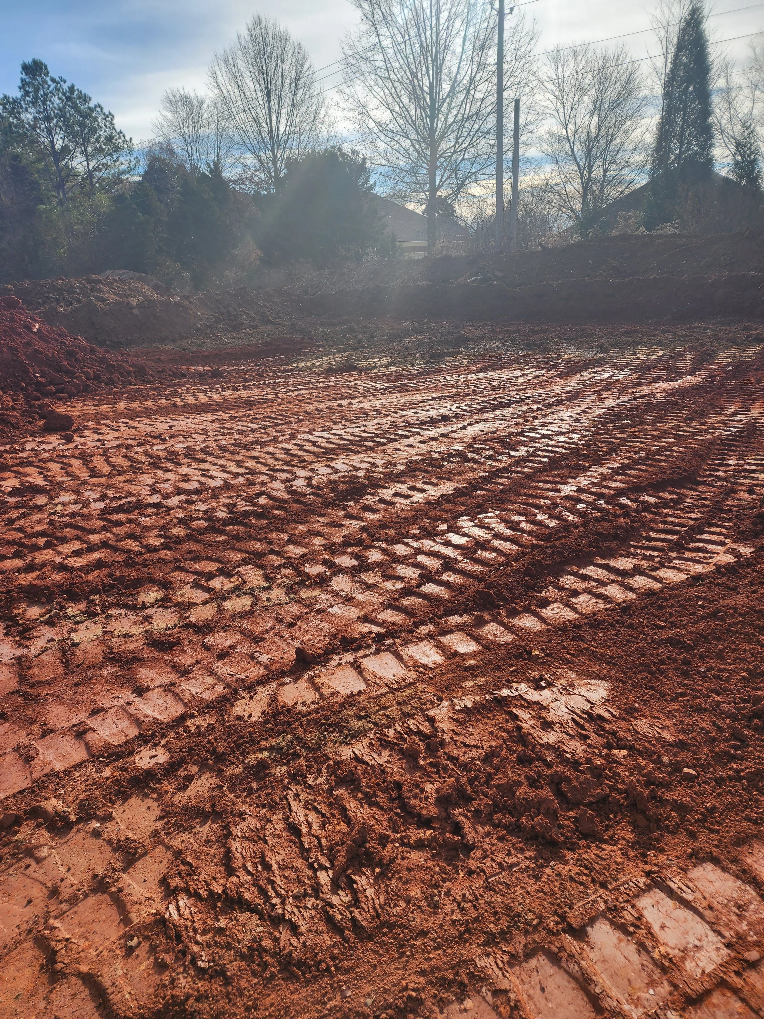 Freshly excavated and graded residential lot with red clay soil and equipment tracks