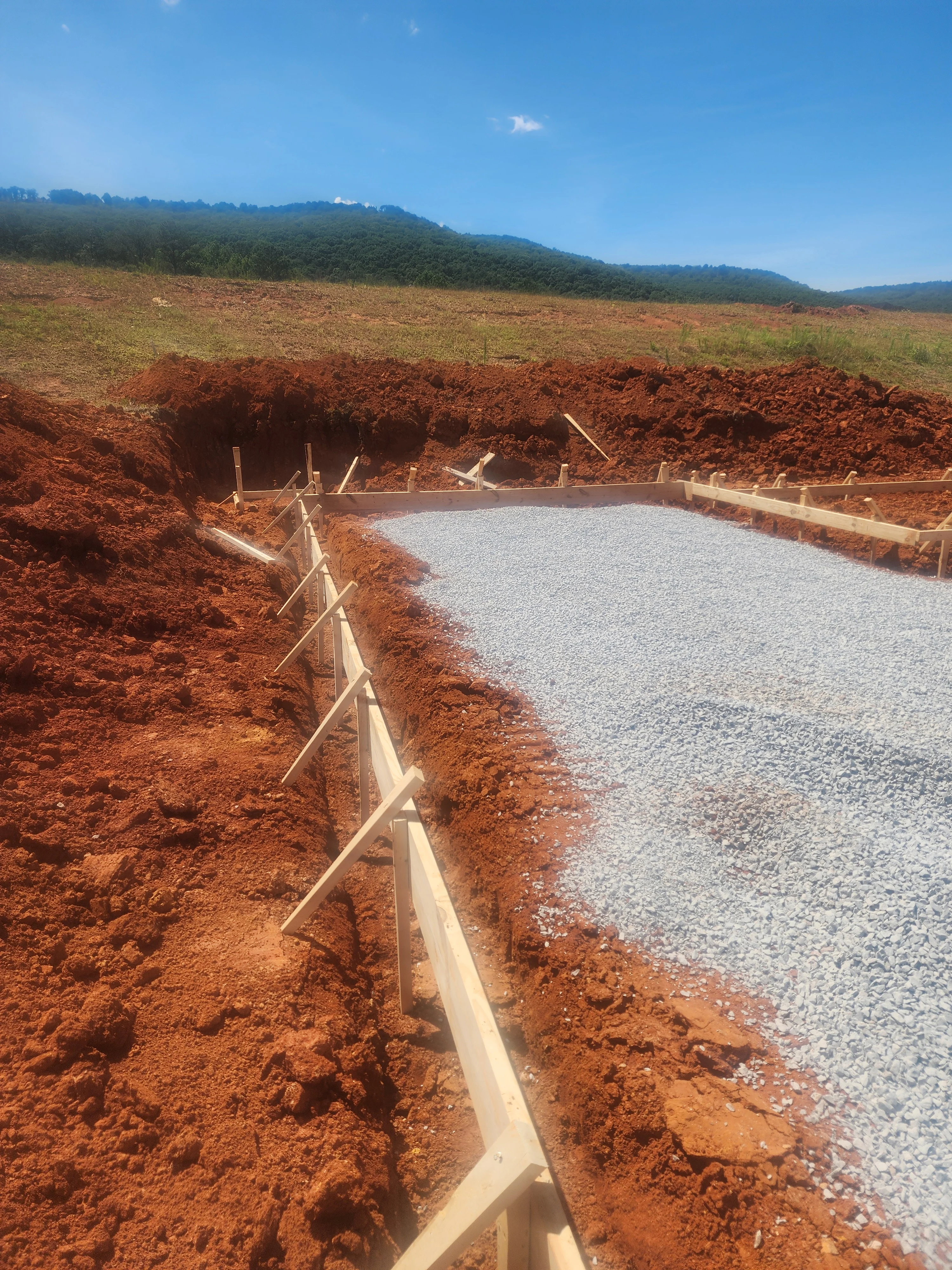 Excavated foundation pit with concrete forms and gravel base in rural Alabama setting