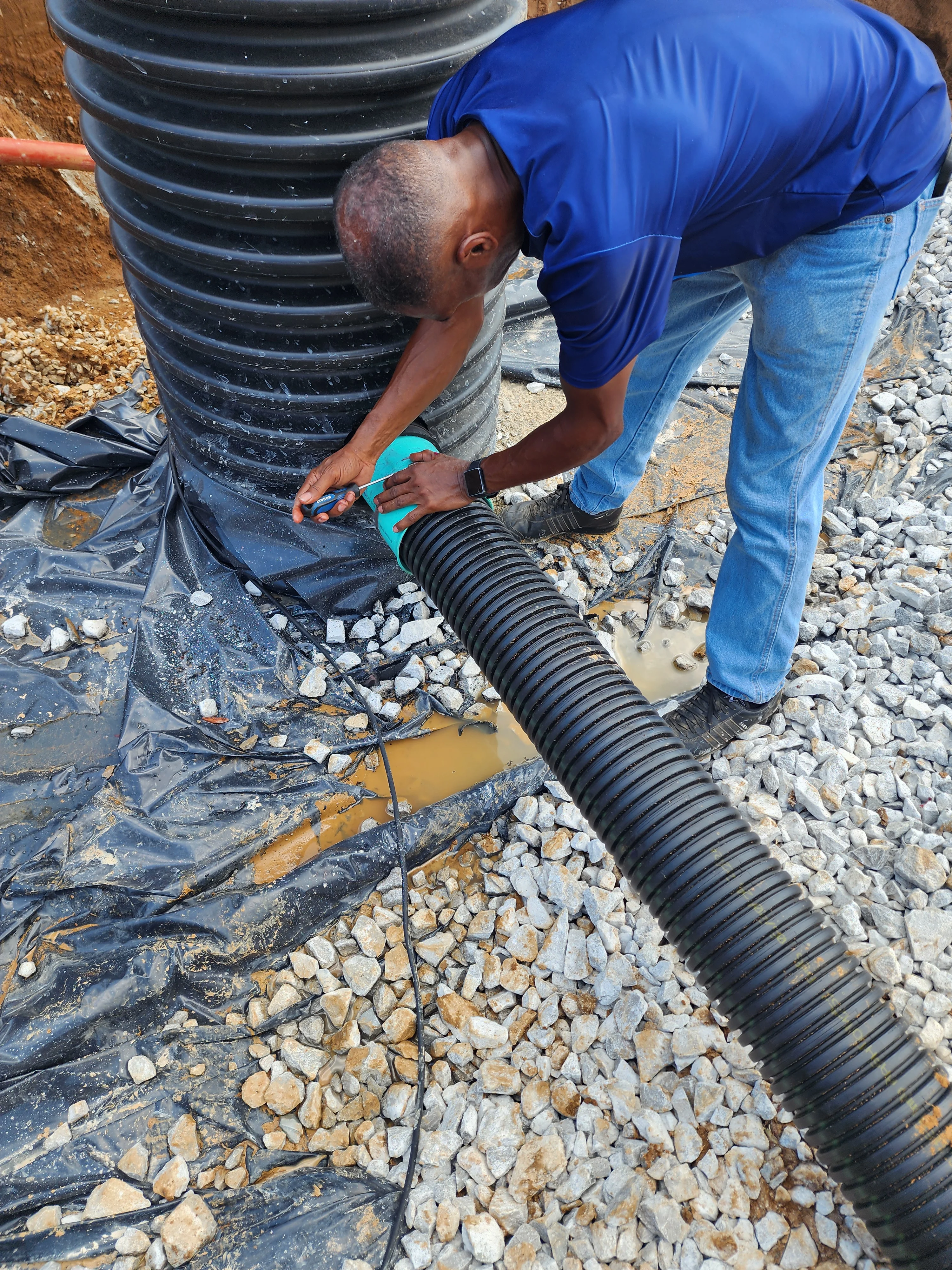 Technician installing black corrugated drainage pipe with gravel base and landscape fabric