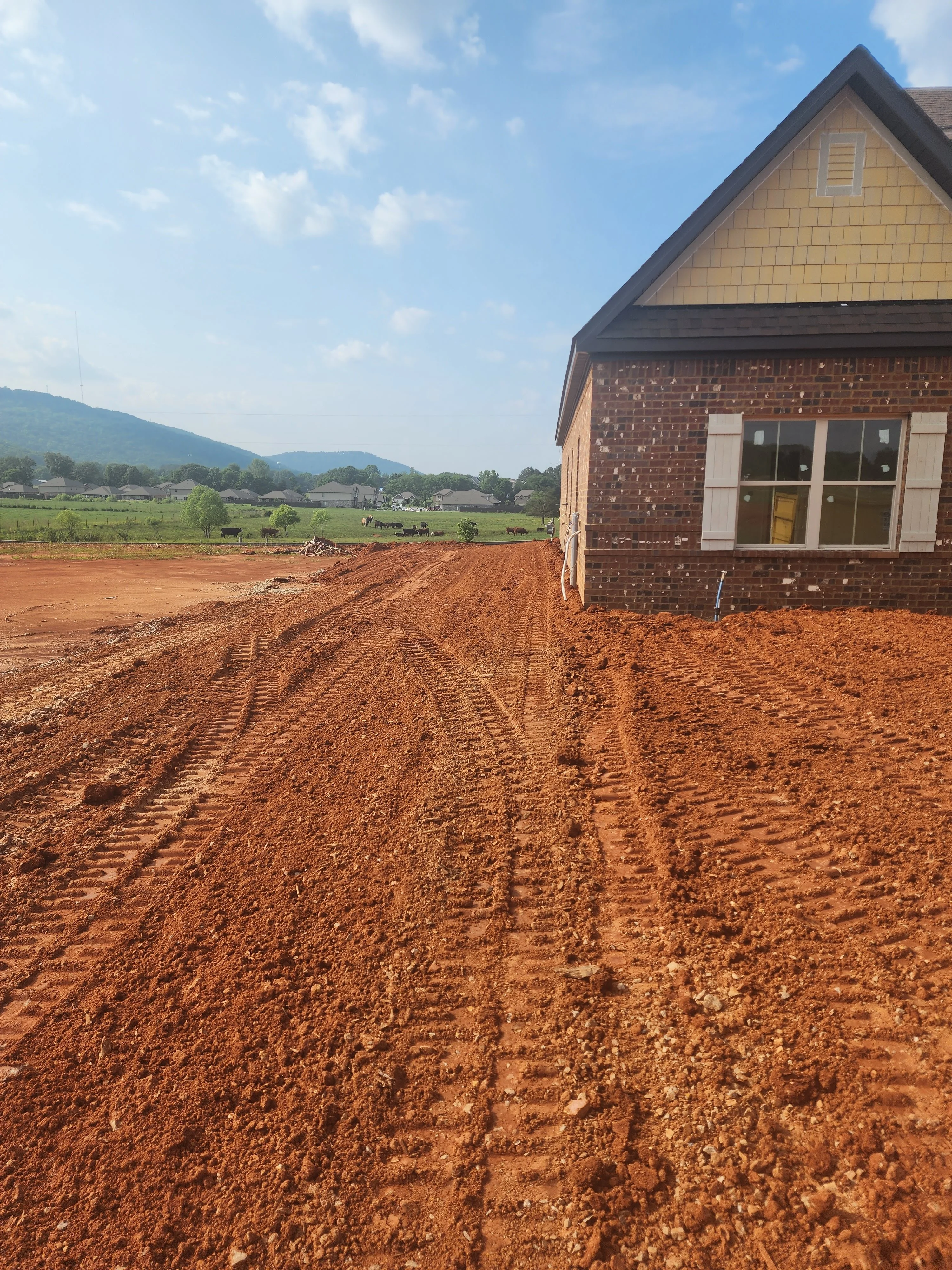 Newly excavated and graded residential lot with brick home and mountain backdrop