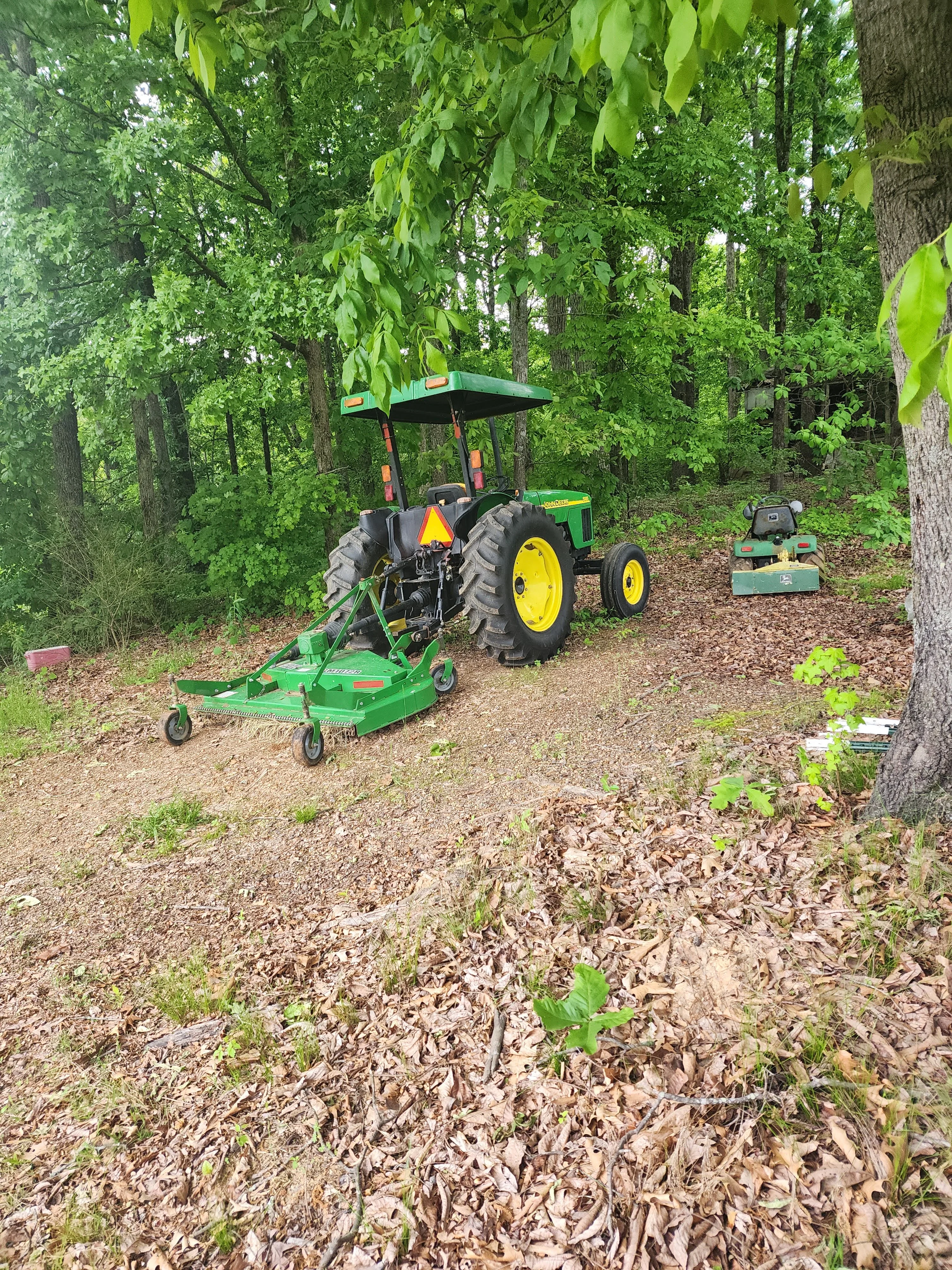 Green John Deere tractor with canopy and mower attachment clearing wooded land