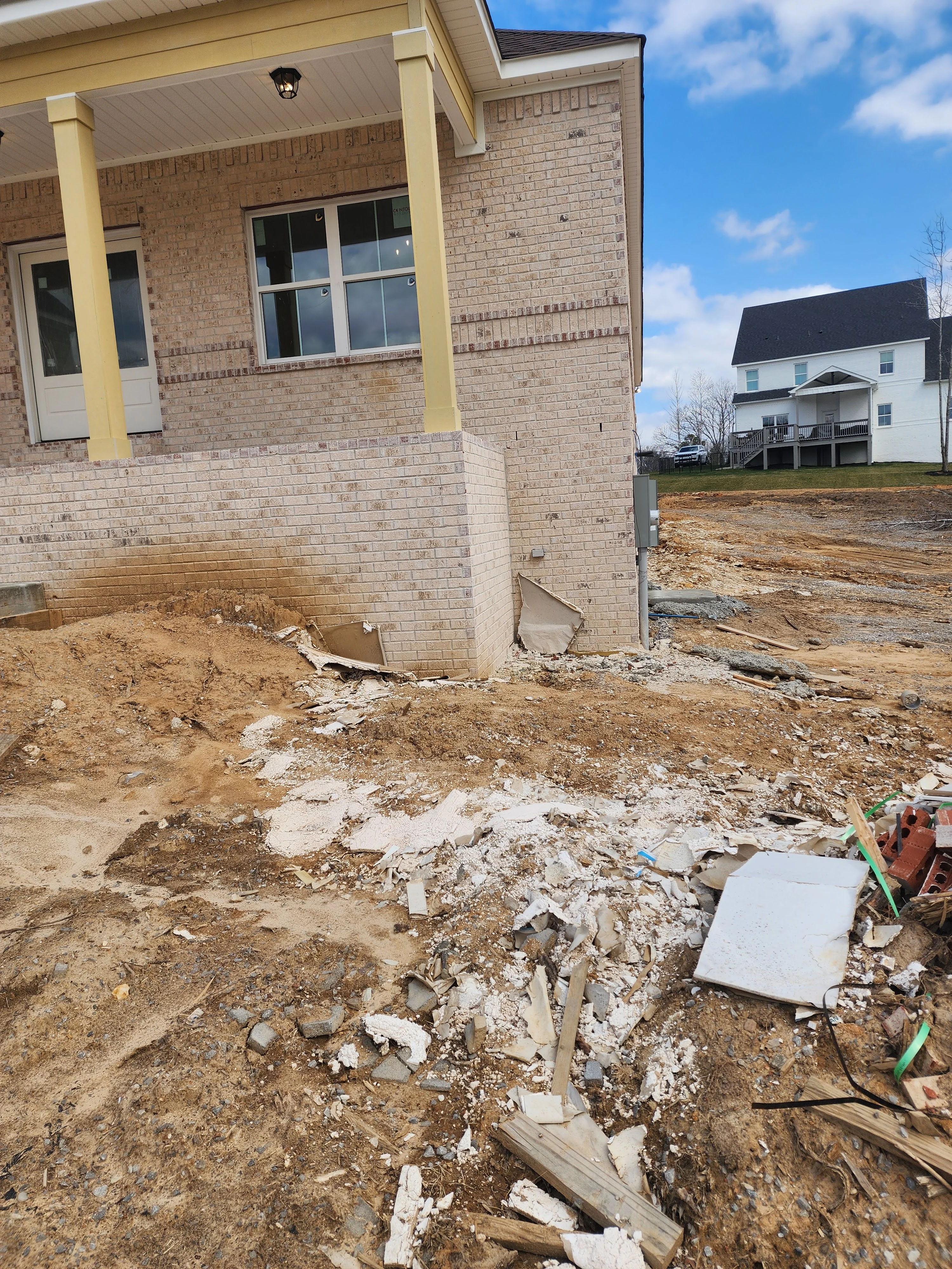 Brick home foundation excavation with cleared site, concrete footings, and yellow support columns