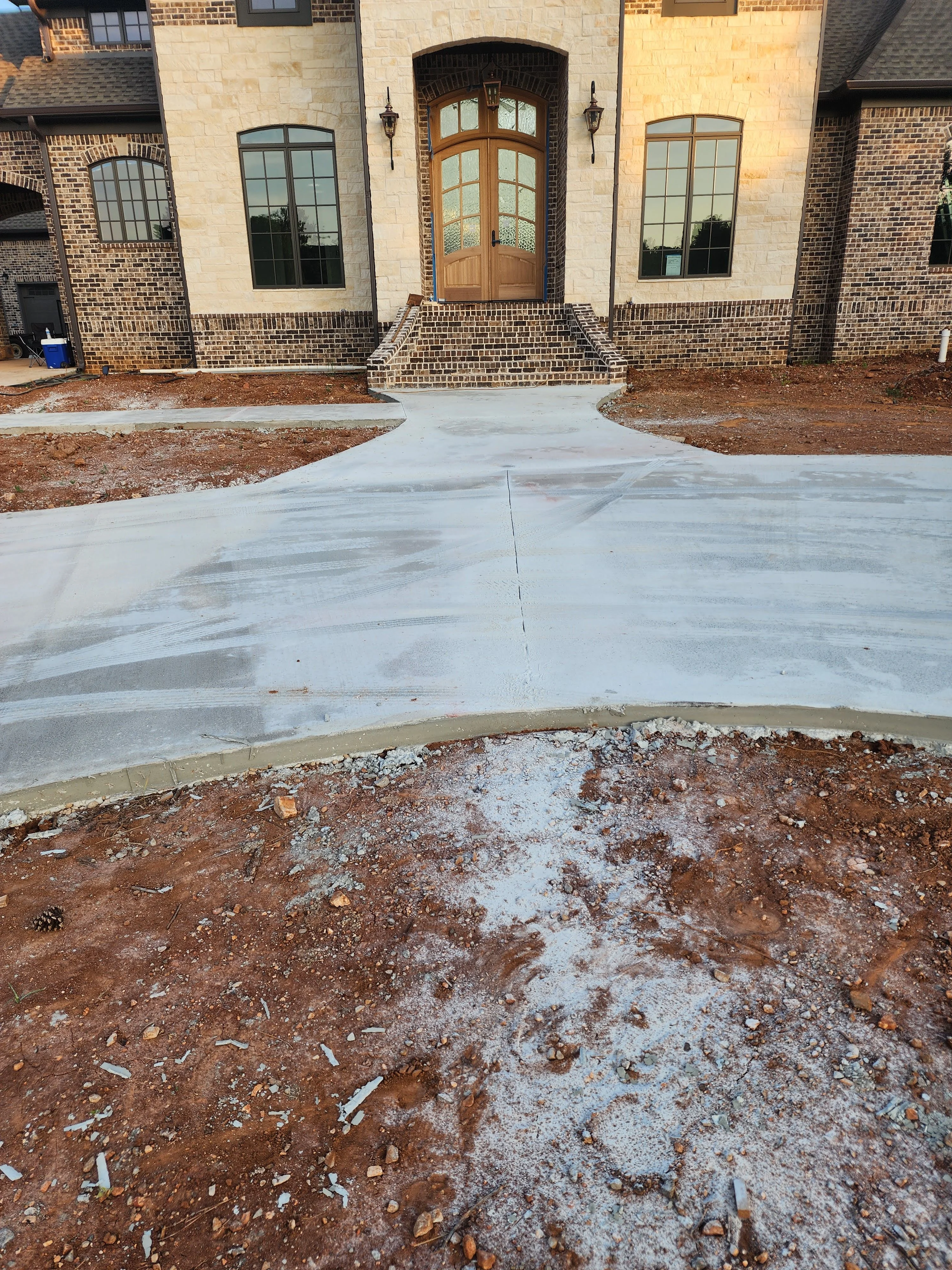 Newly poured concrete driveway with brick home and prepared soil base visible