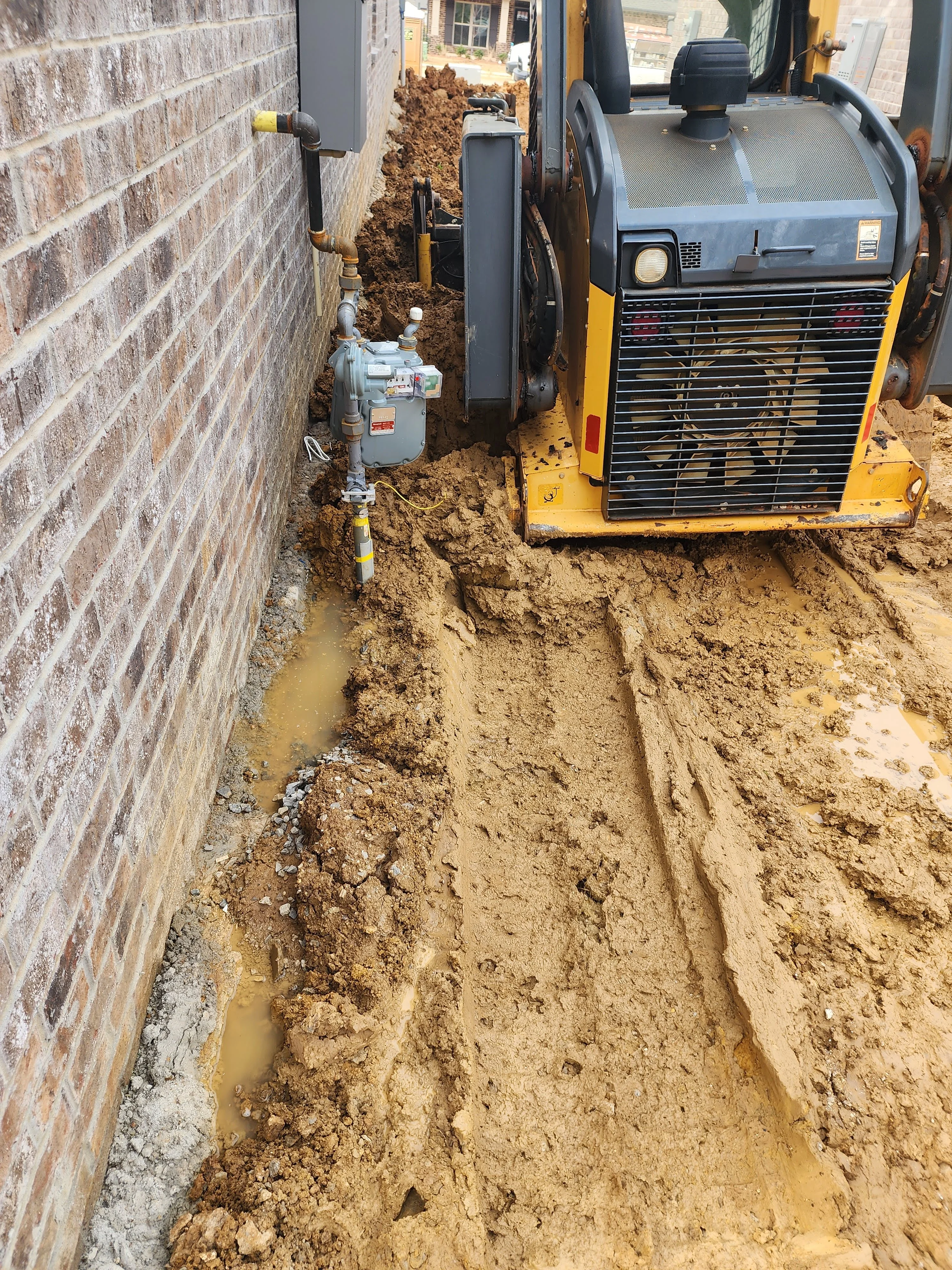 Excavation site with yellow equipment, exposed soil, brick wall, and installed gas meter