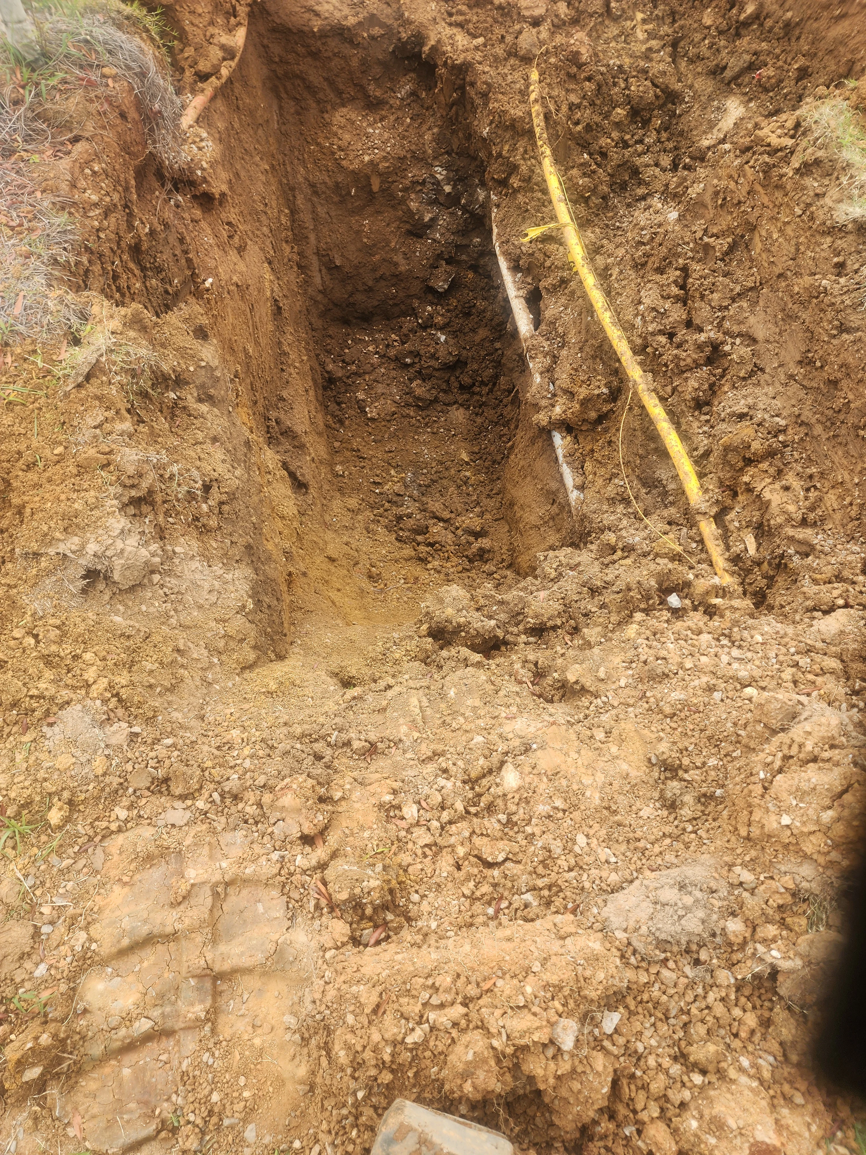 Deep utility trench with squared walls and yellow depth measurement tape
