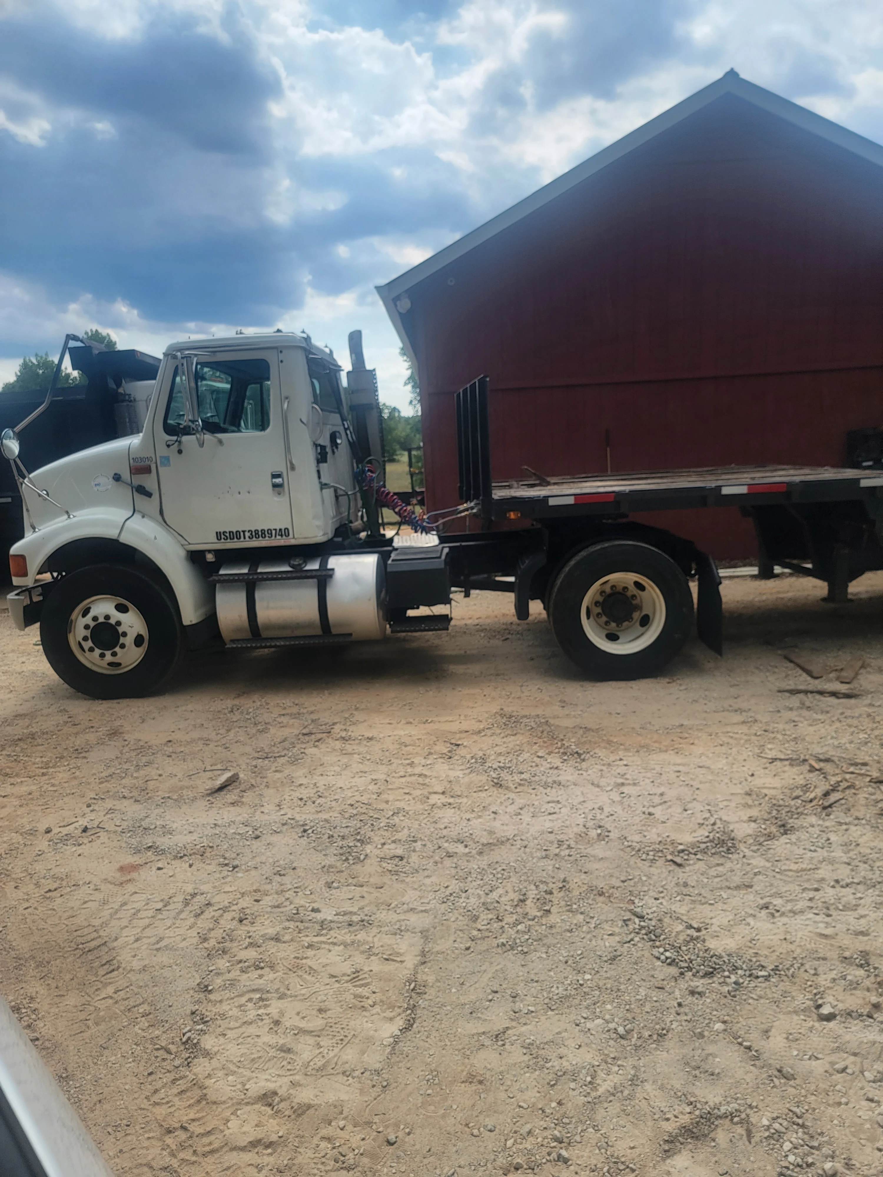 White Isuzu dump truck with red flatbed trailer on dirt lot