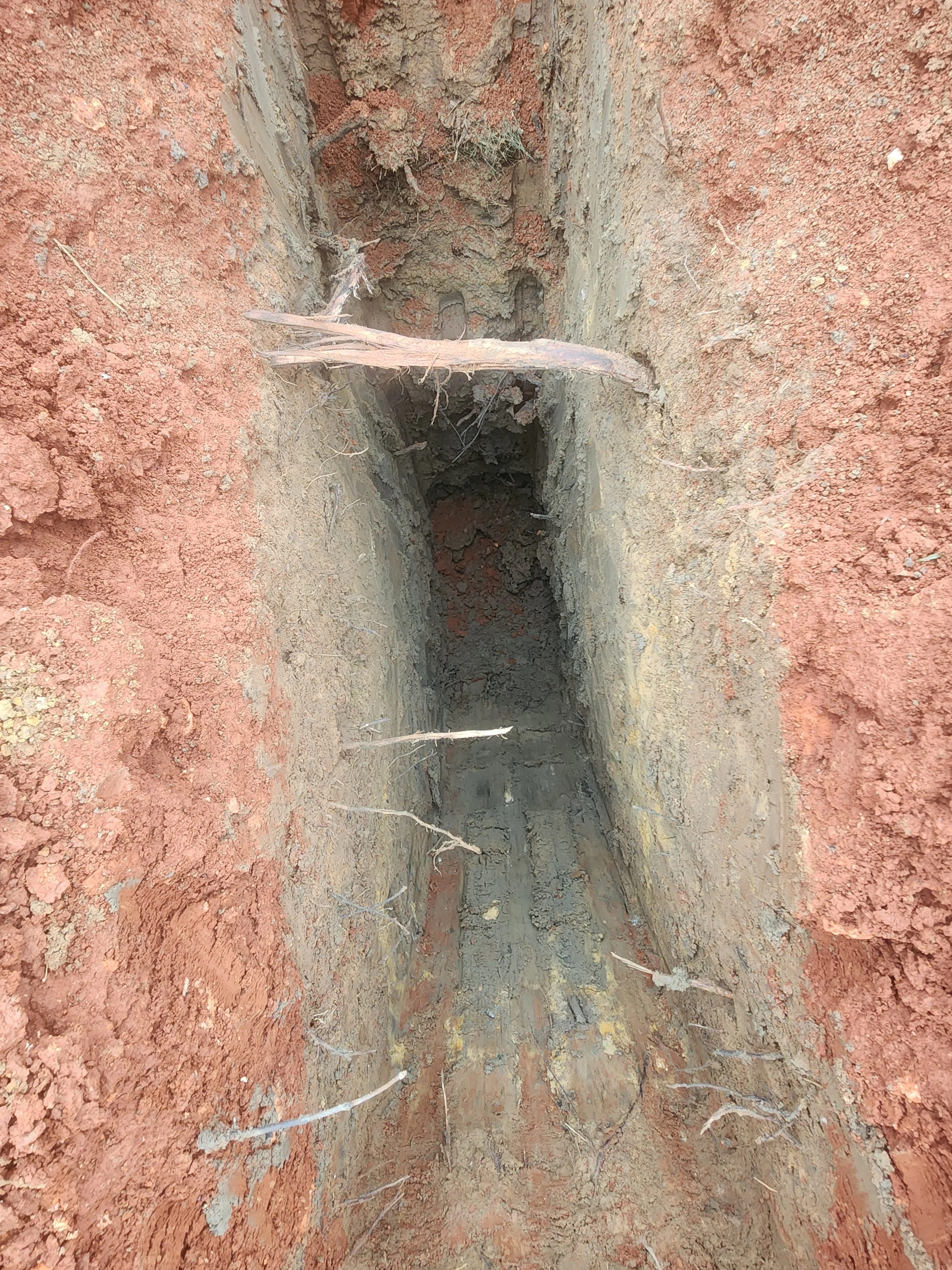 Deep concrete-lined utility trench with vertical walls in red clay soil