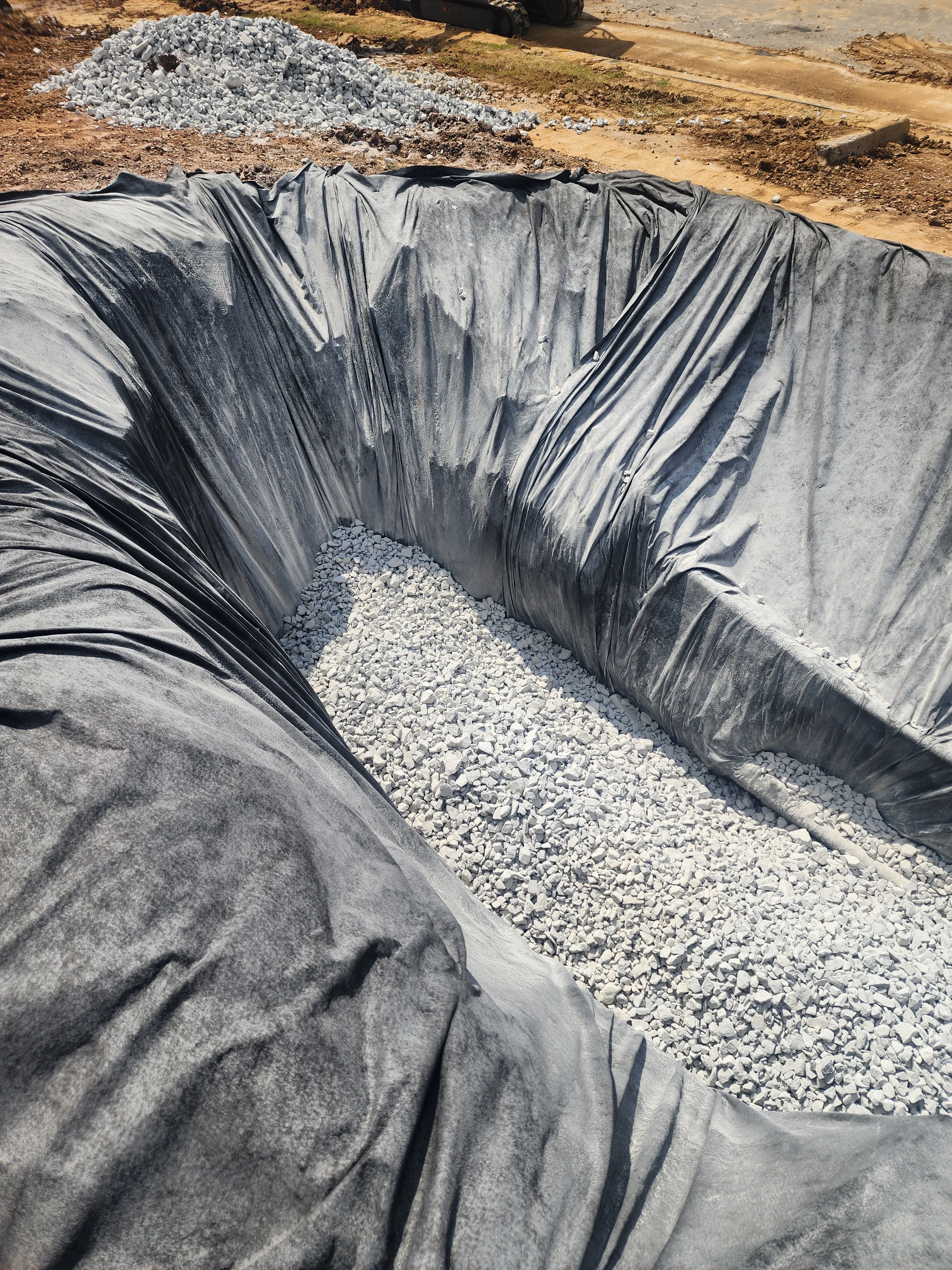 Lined trench with white gravel base and black landscape fabric erosion control