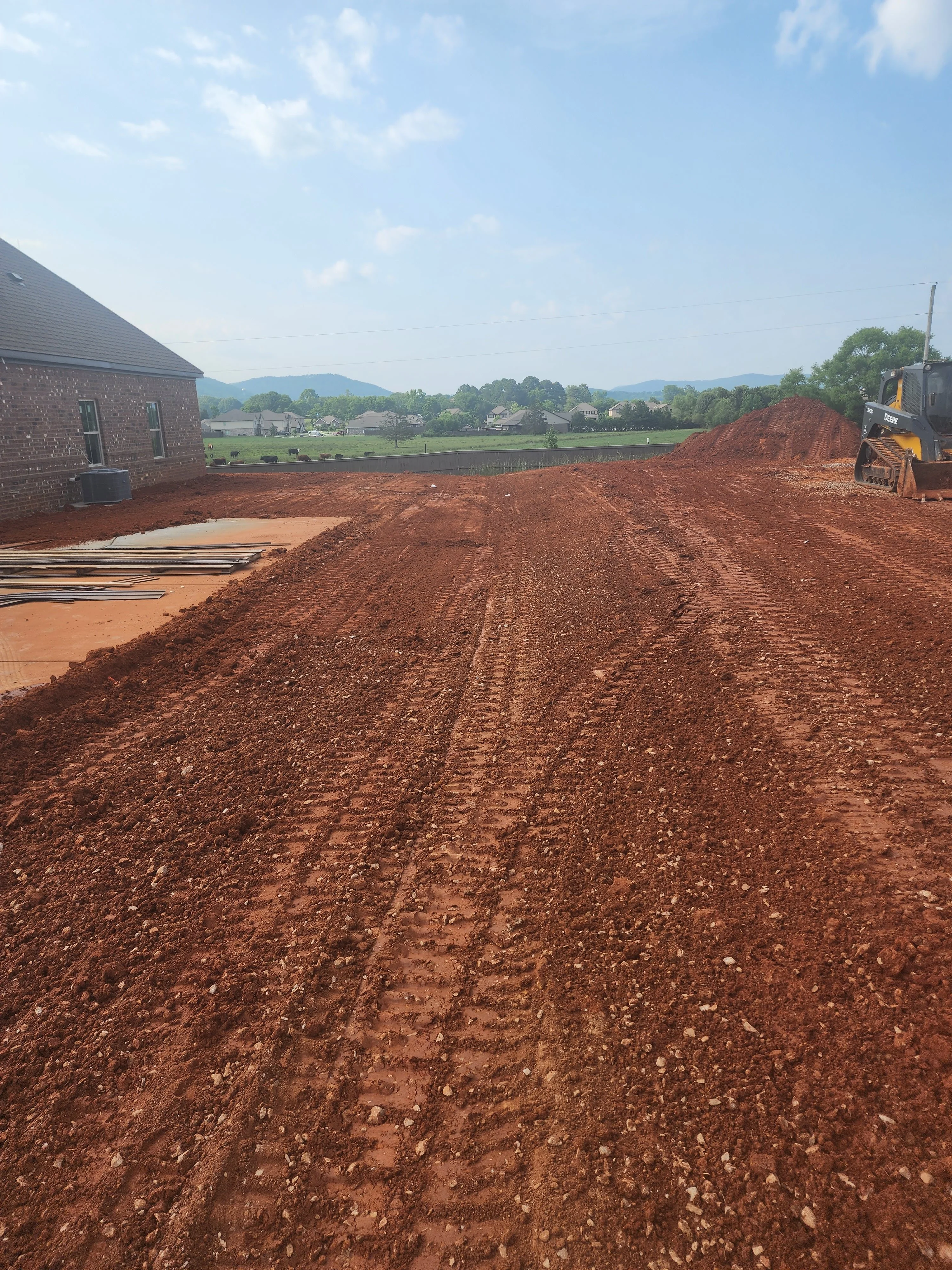 Red clay excavation site with skid steer loader and brick home in rural Alabama setting