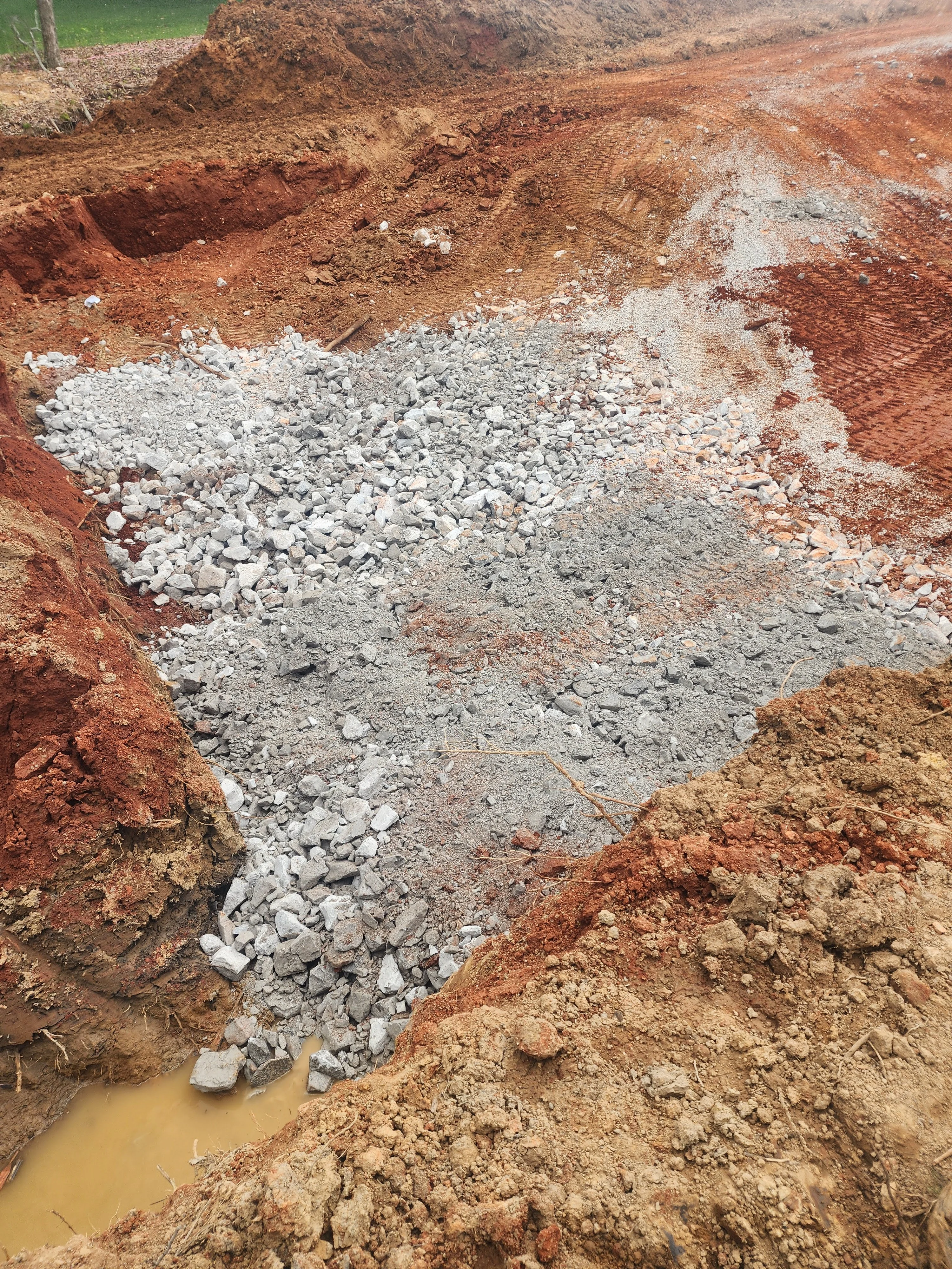 Excavated site with white crushed limestone base and red clay soil layers