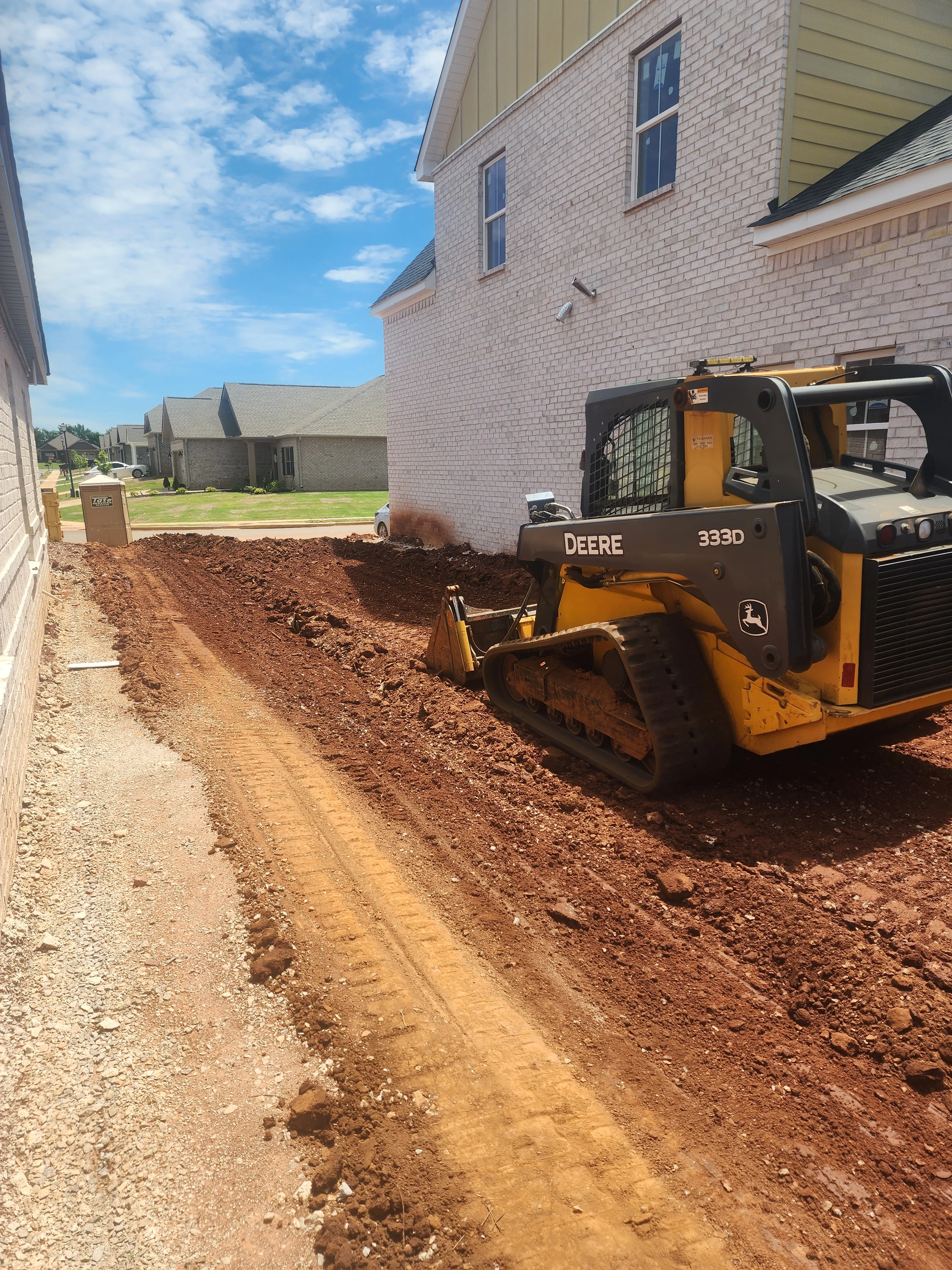 Deere 333D compact track loader grading residential driveway with clay soil at brick home site