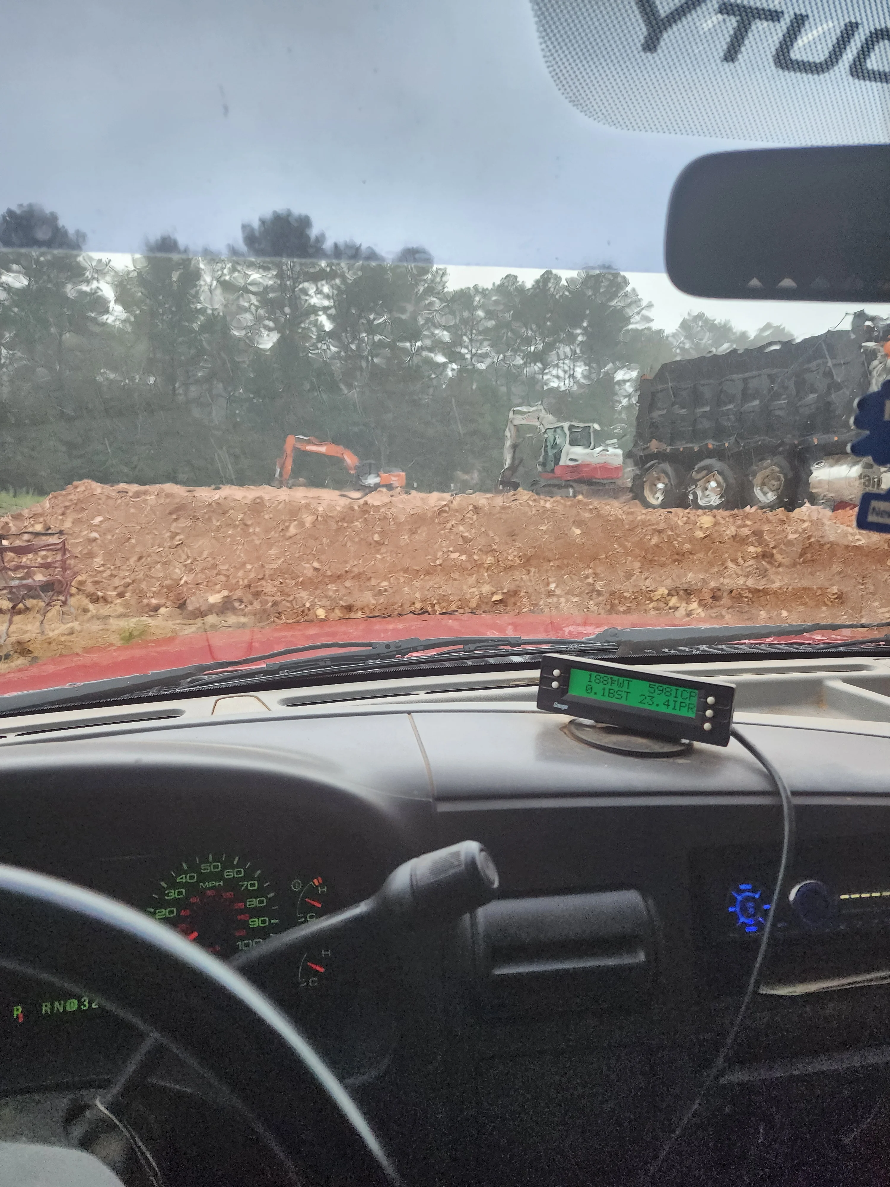 Excavation site with orange excavator and dump trucks loading material on cleared dirt lot