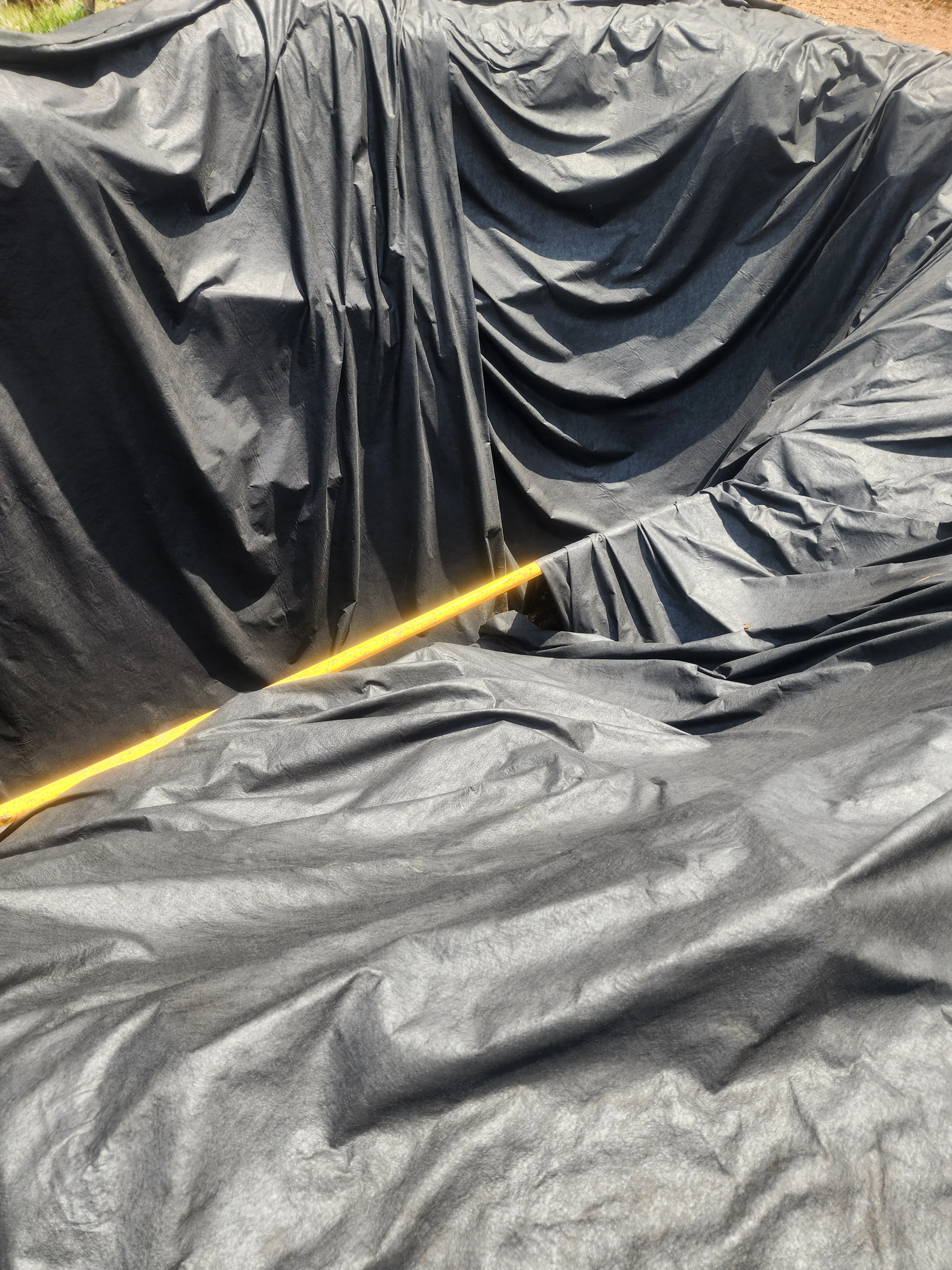 Black HDPE pond liner installed in excavated basin with yellow rope alignment marker