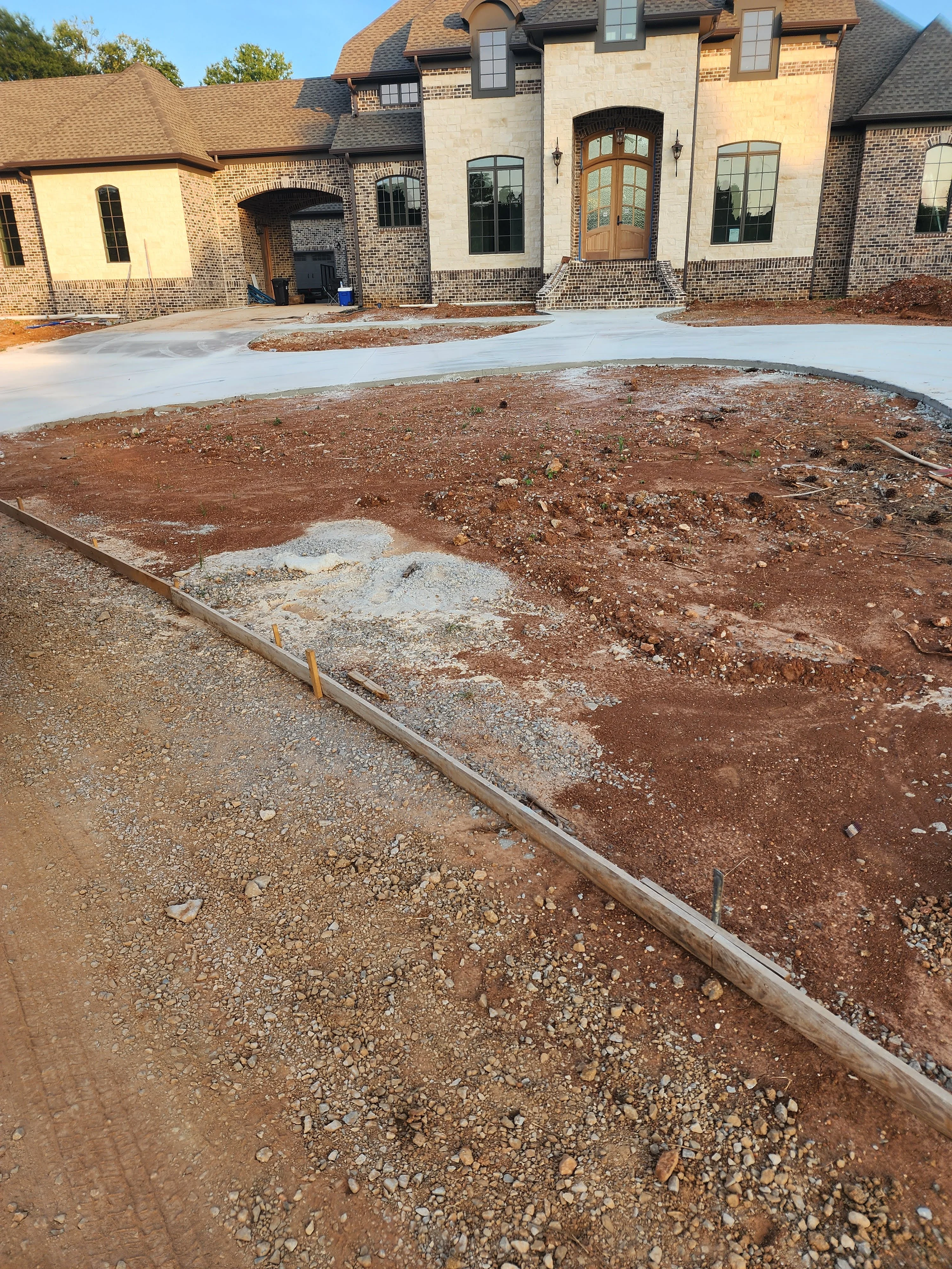 Residential excavation site with prepared soil, concrete driveway, and brick home under construction
