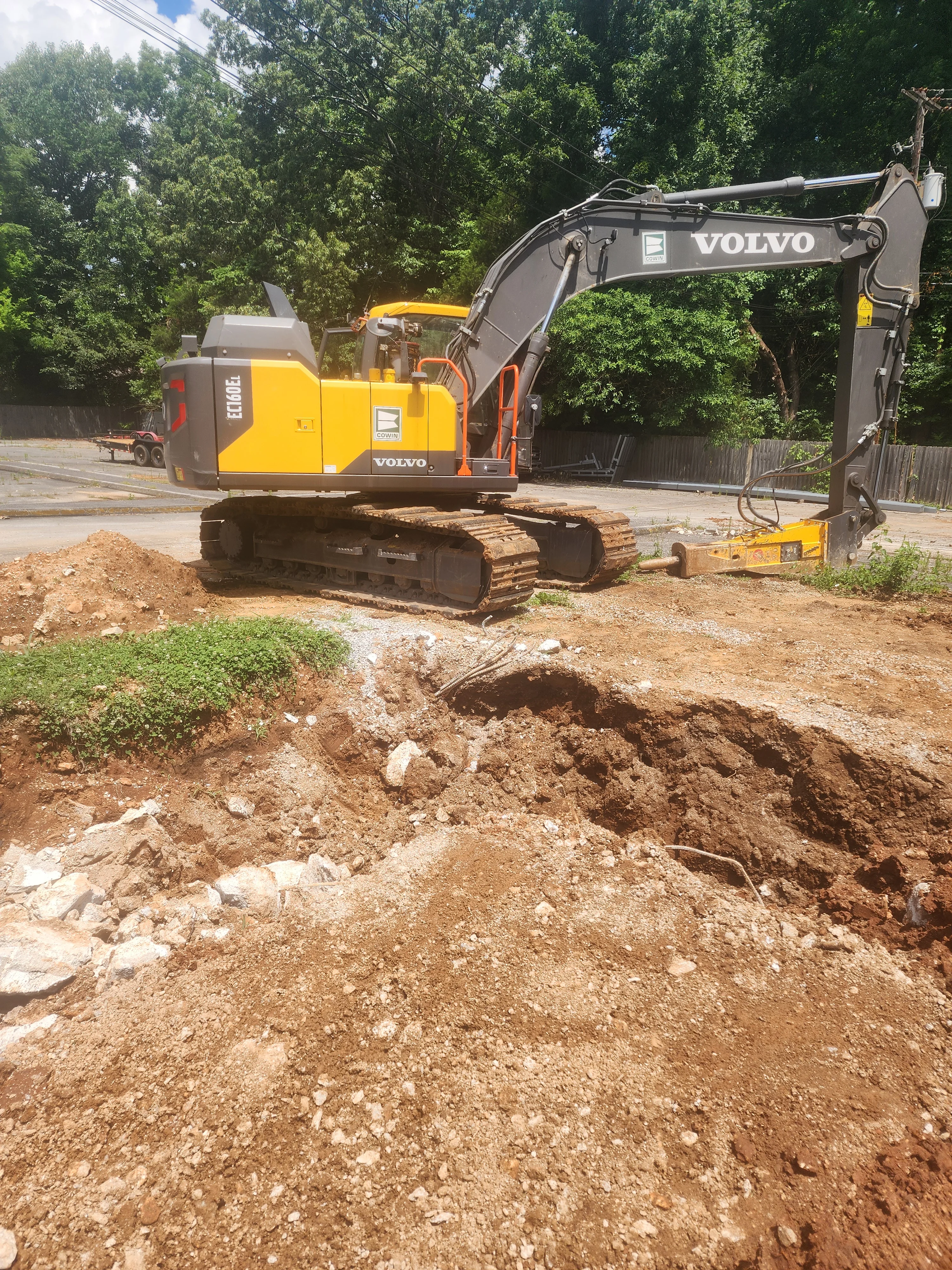 Yellow and gray Volvo excavator on tracked chassis performing soil excavation at residential site