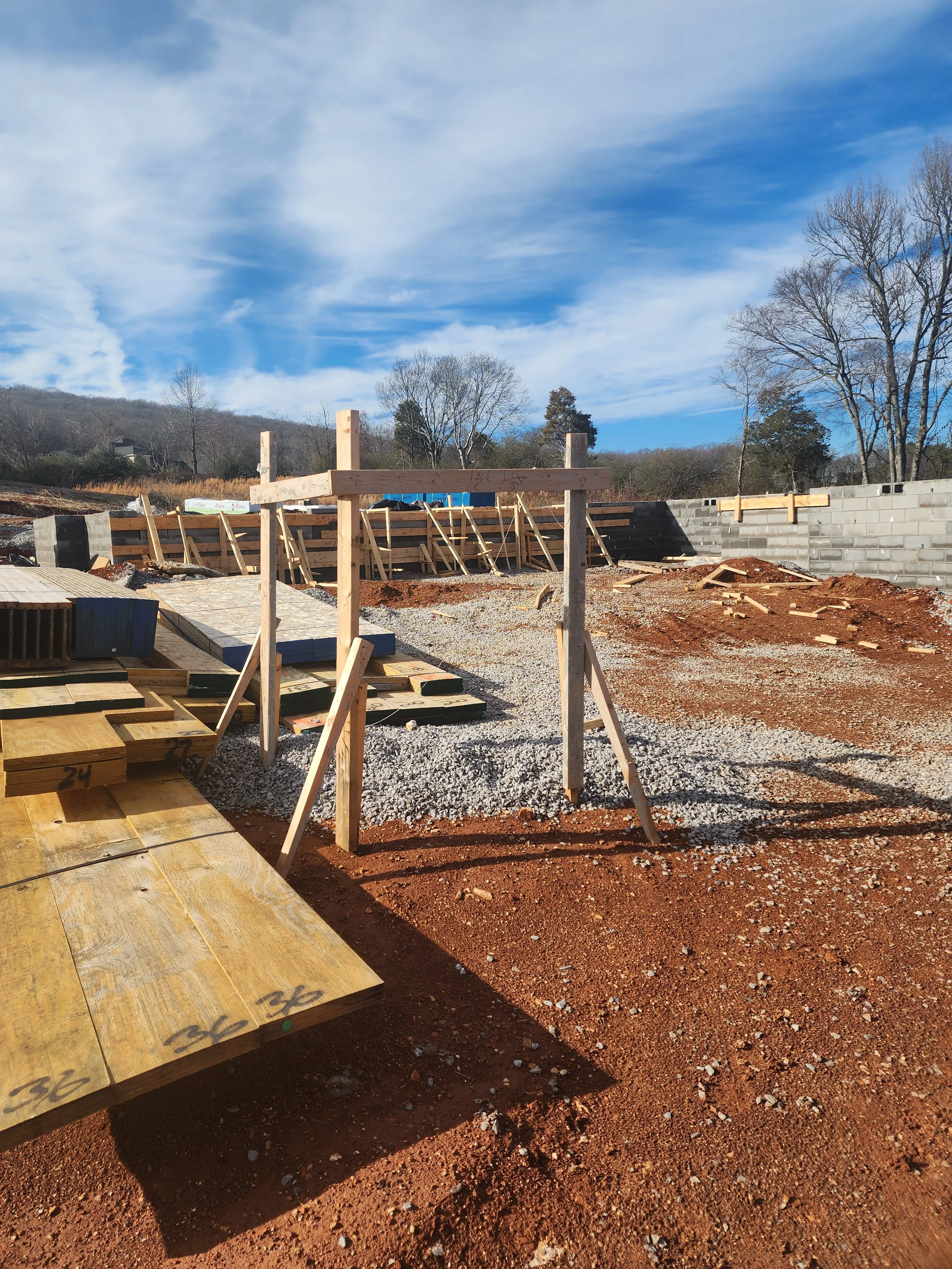 Active construction site with timber framing, gravel base, and concrete foundation walls under clear sky
