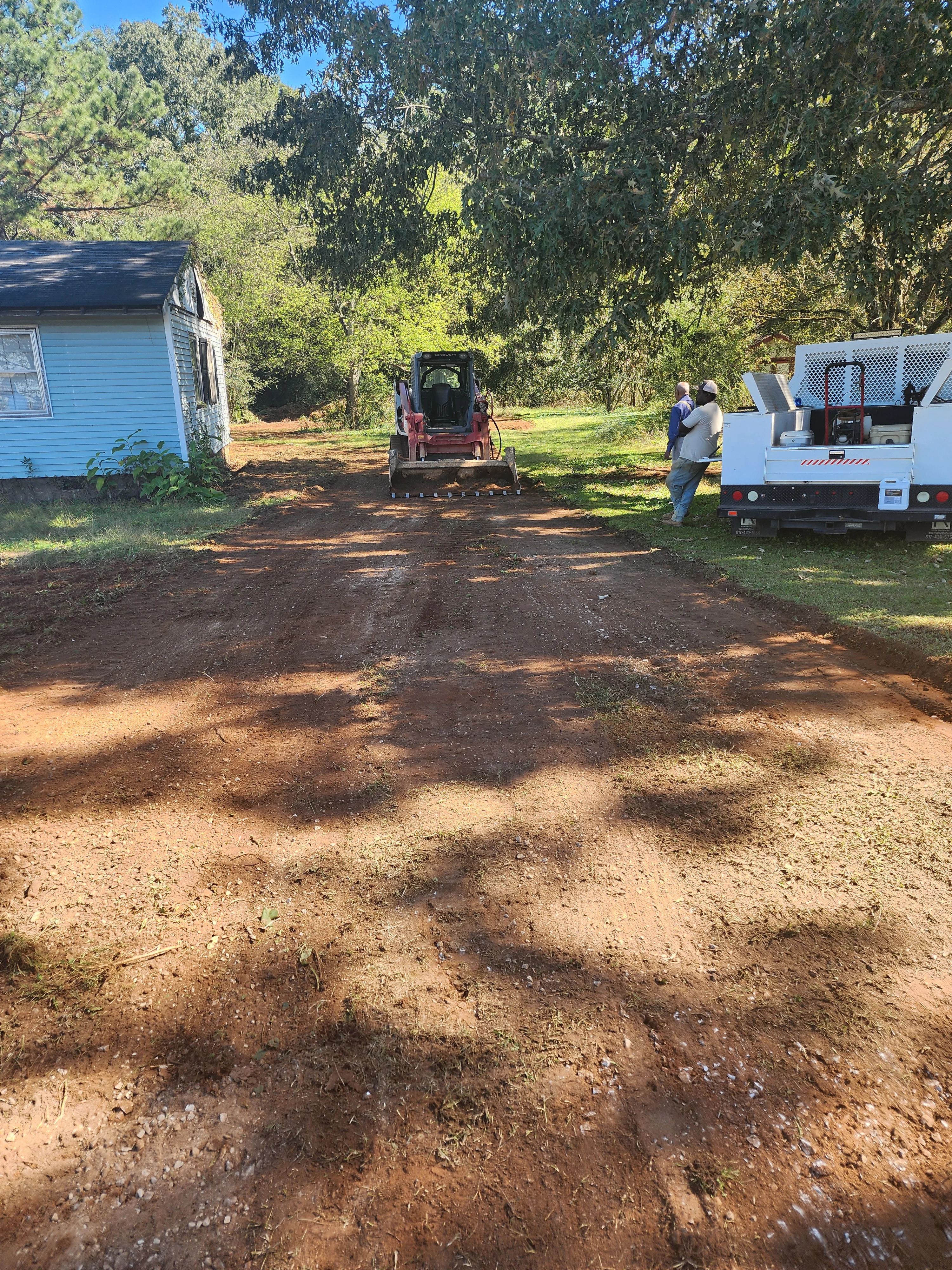 Compact track loader grading residential driveway with red clay soil on wooded property