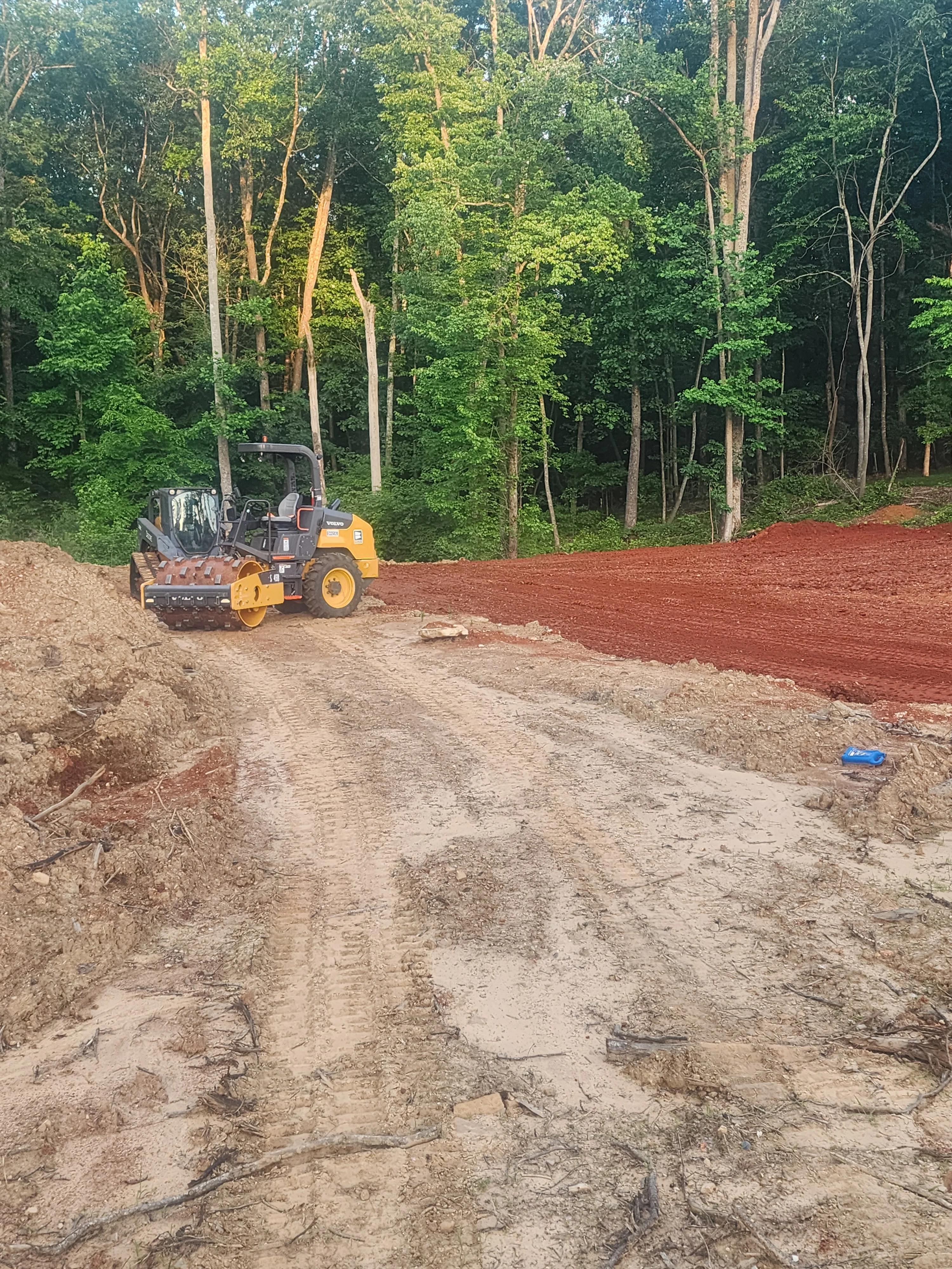Yellow vibratory roller compacting red clay on residential driveway excavation site