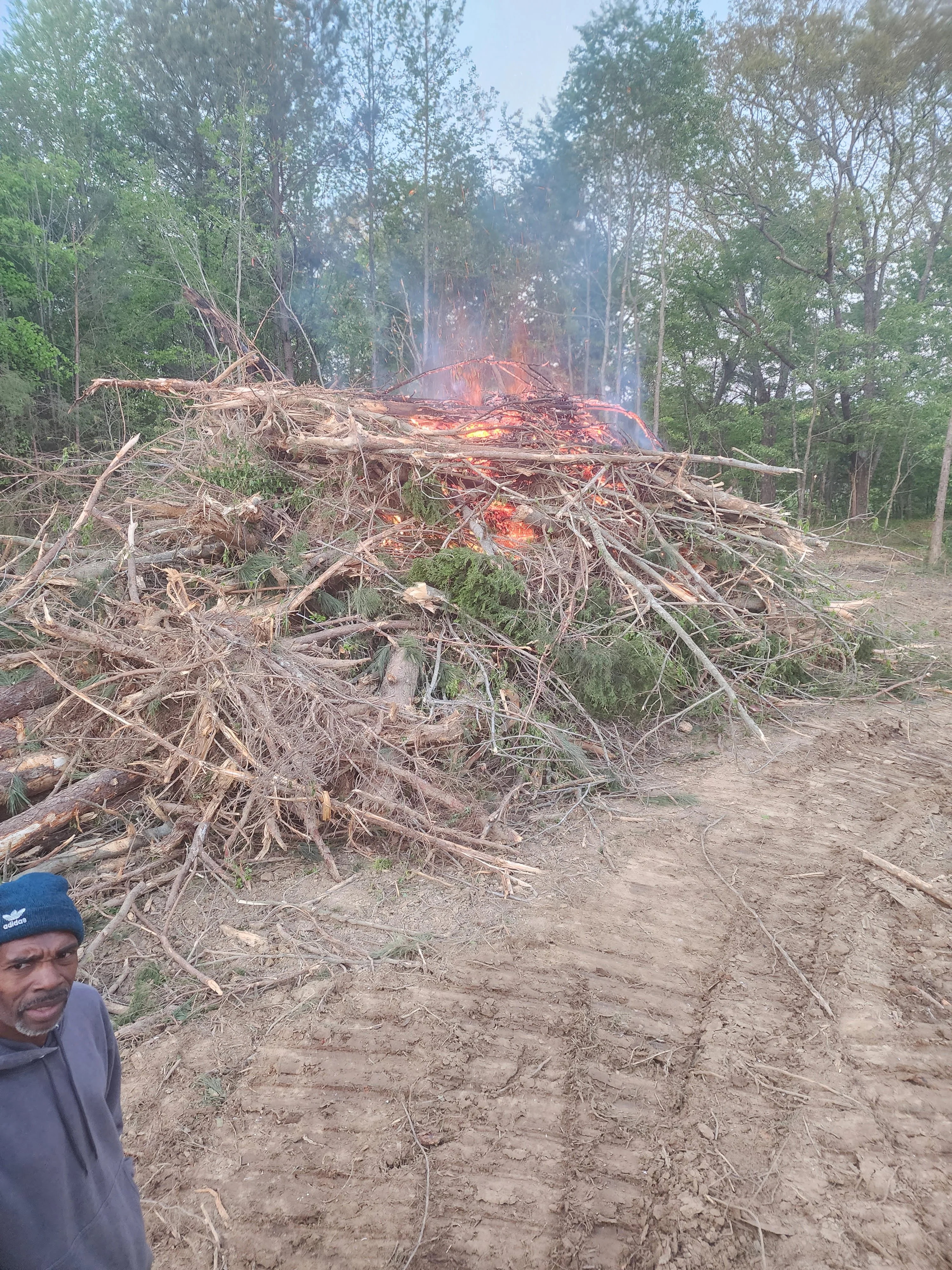 Land clearing operation with burning debris pile and surrounding forest in Toney, AL
