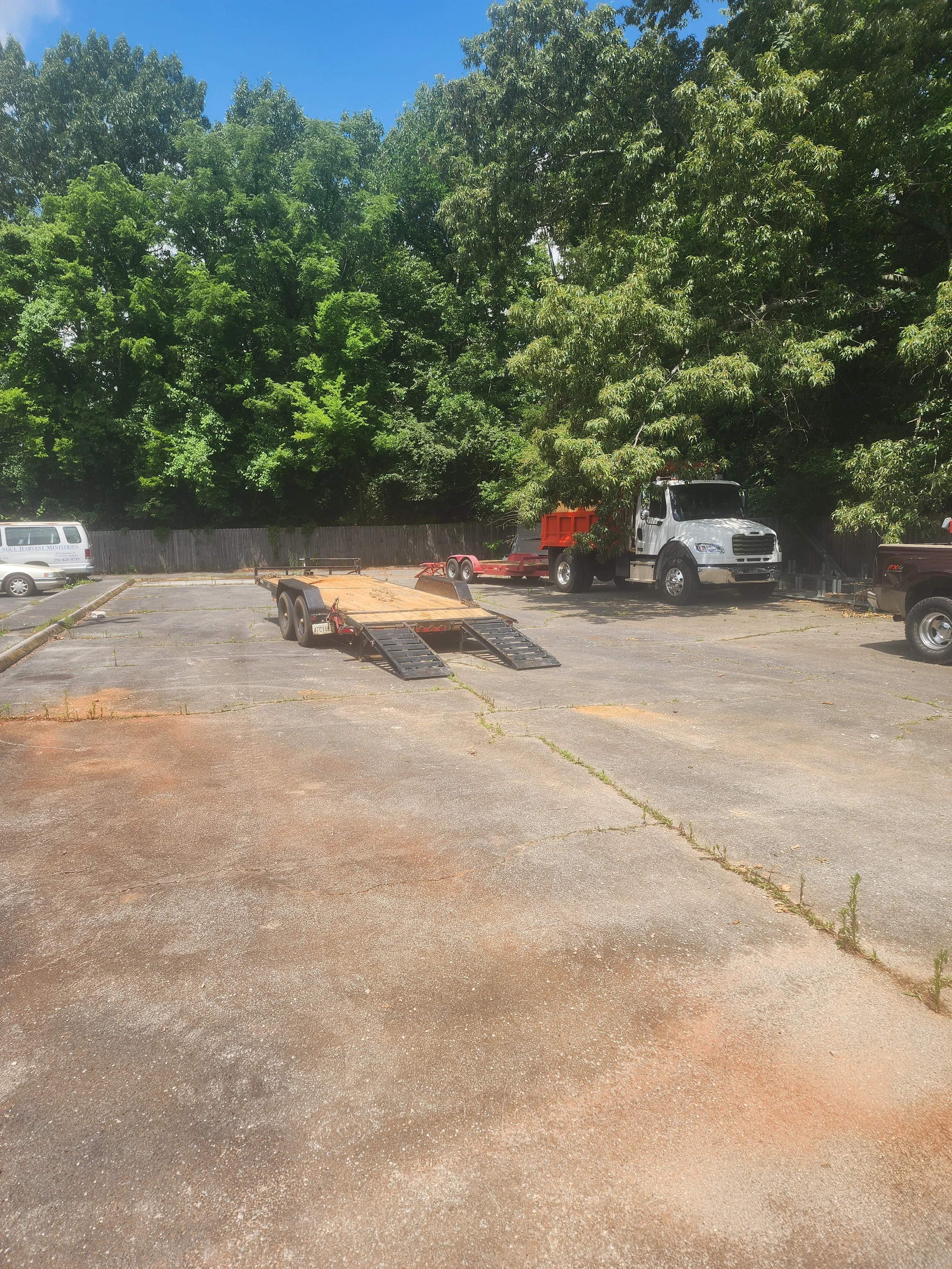 Equipment yard with trailers, white truck, and cleared dirt surface surrounded by trees