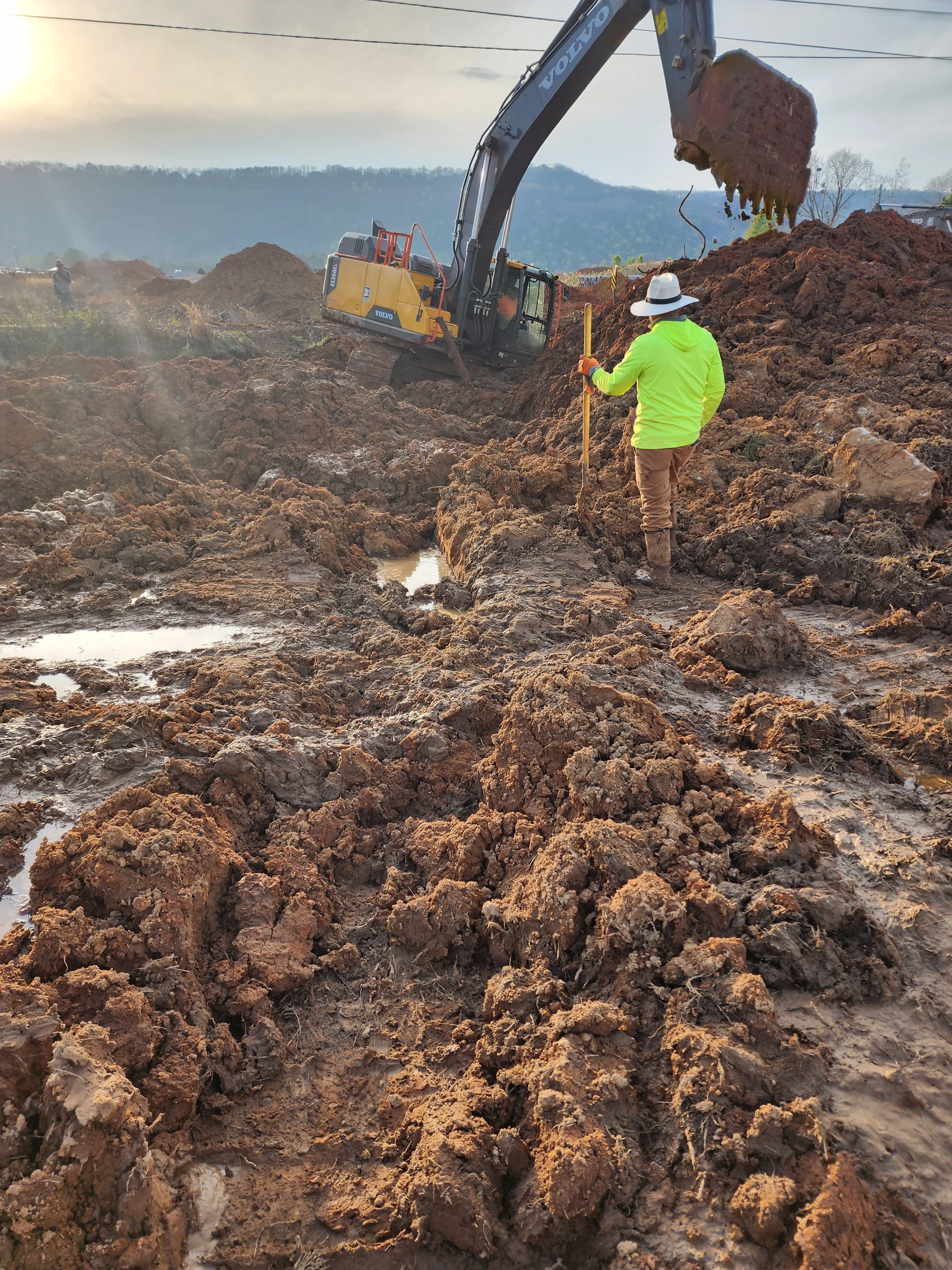 Excavator moving earth material on active construction site with surveyor monitoring progress