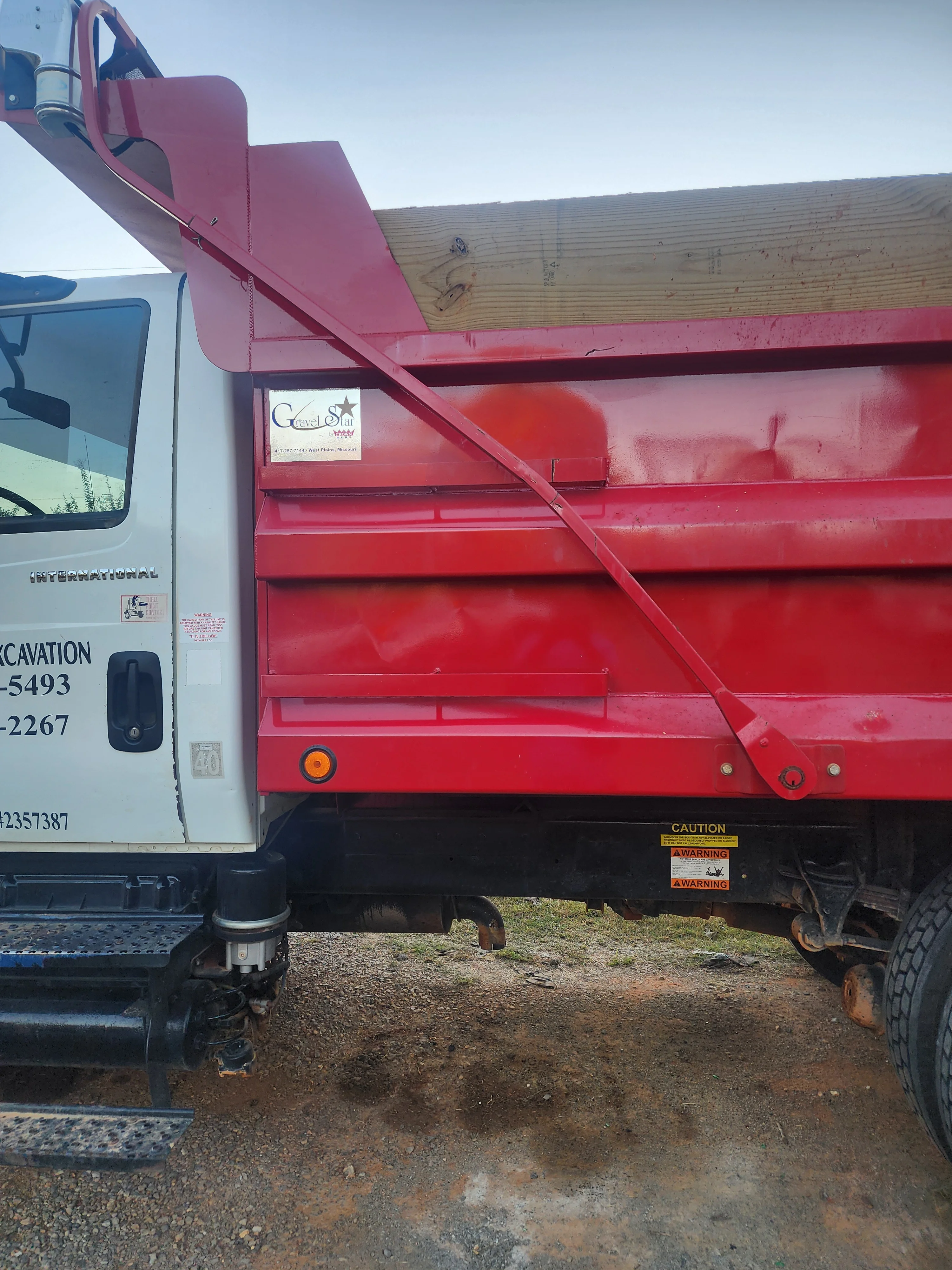 Red hydraulic dump truck with open bed and articulated tailgate for material hauling