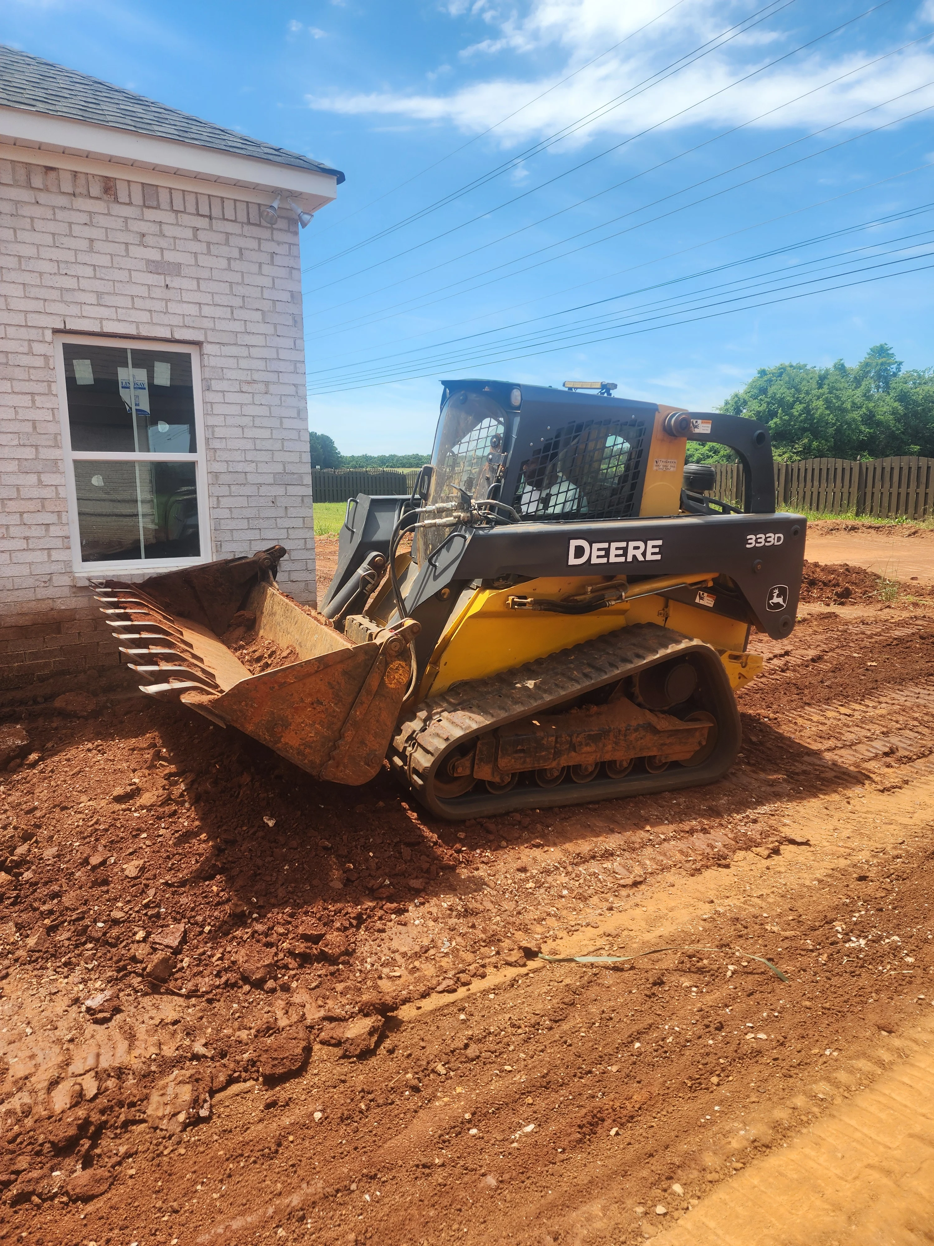 Deere 333D compact track loader excavating red clay soil at residential site in Toney, AL