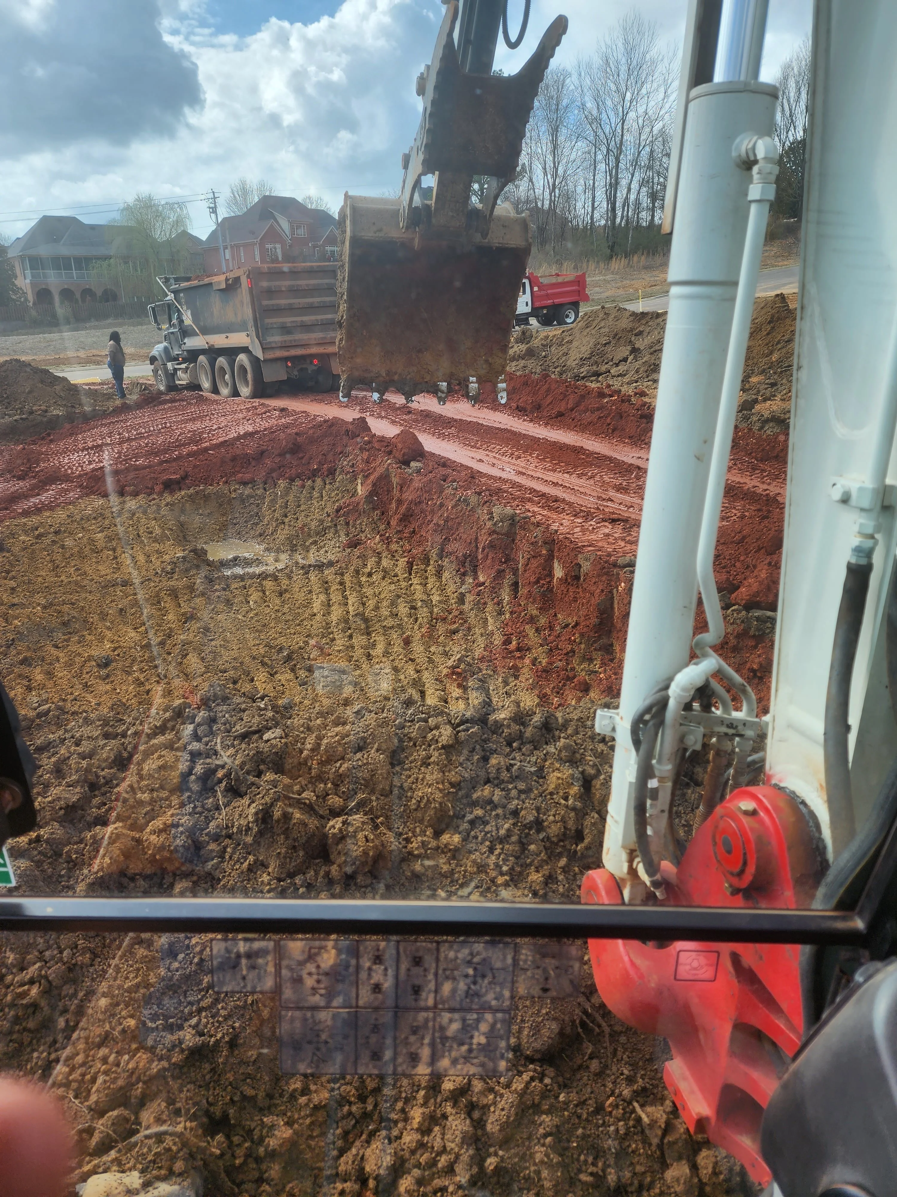 Excavator removing red clay soil from deep foundation pit at residential site