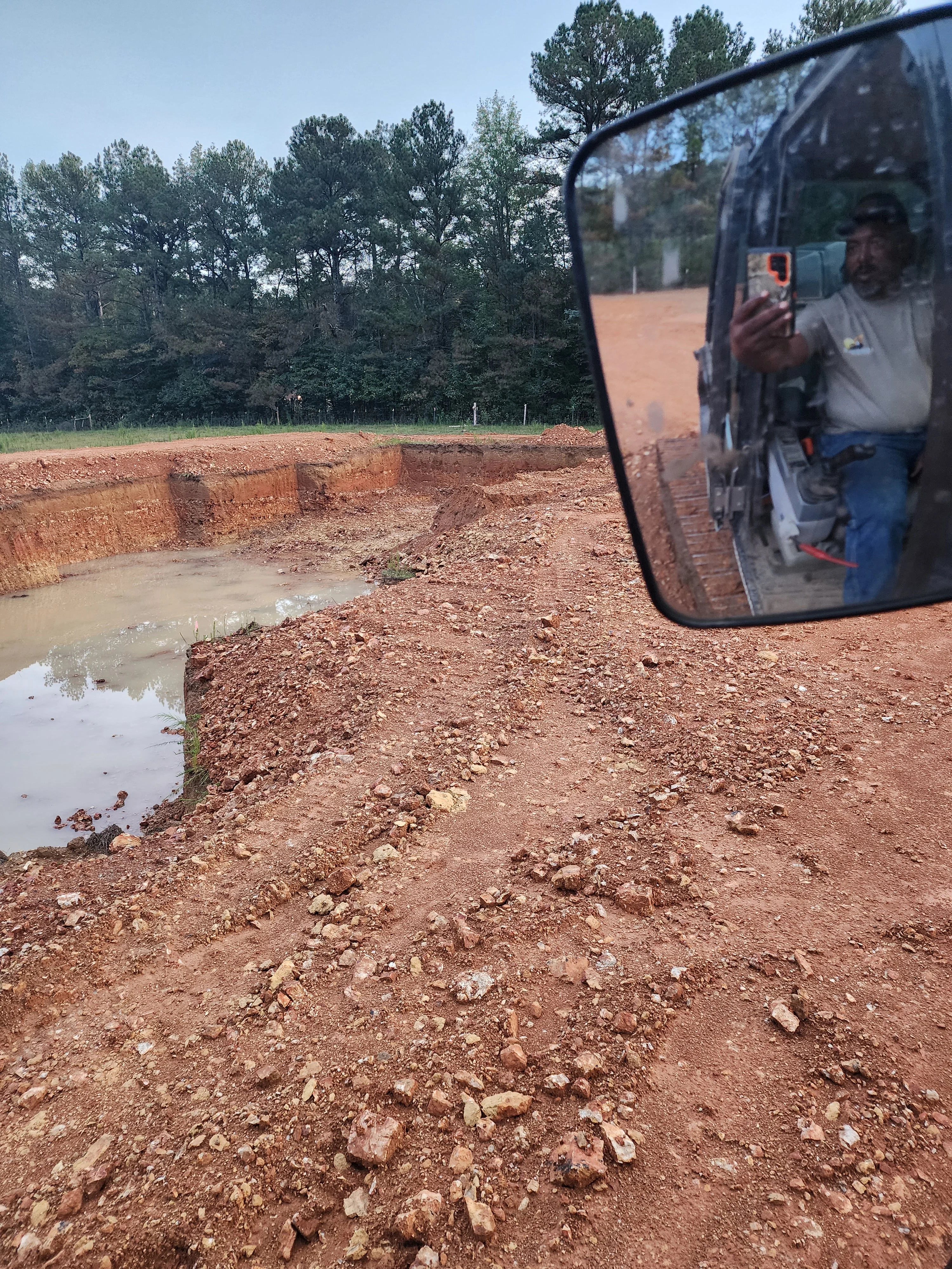 Excavated pond site with clay walls and water pooling at base, forested background
