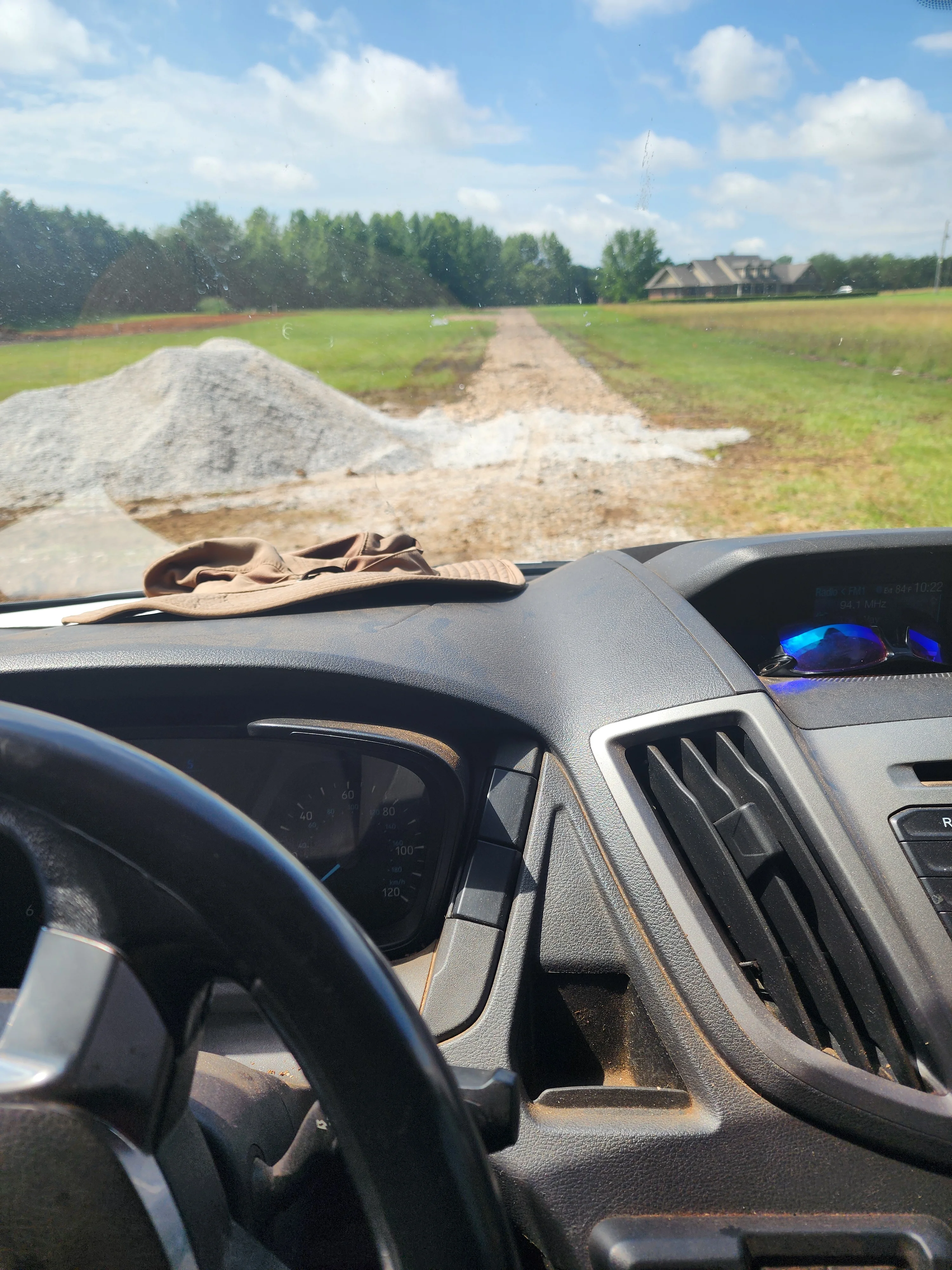 Driveway excavation site with graded earth, crushed stone pile, and rural property backdrop