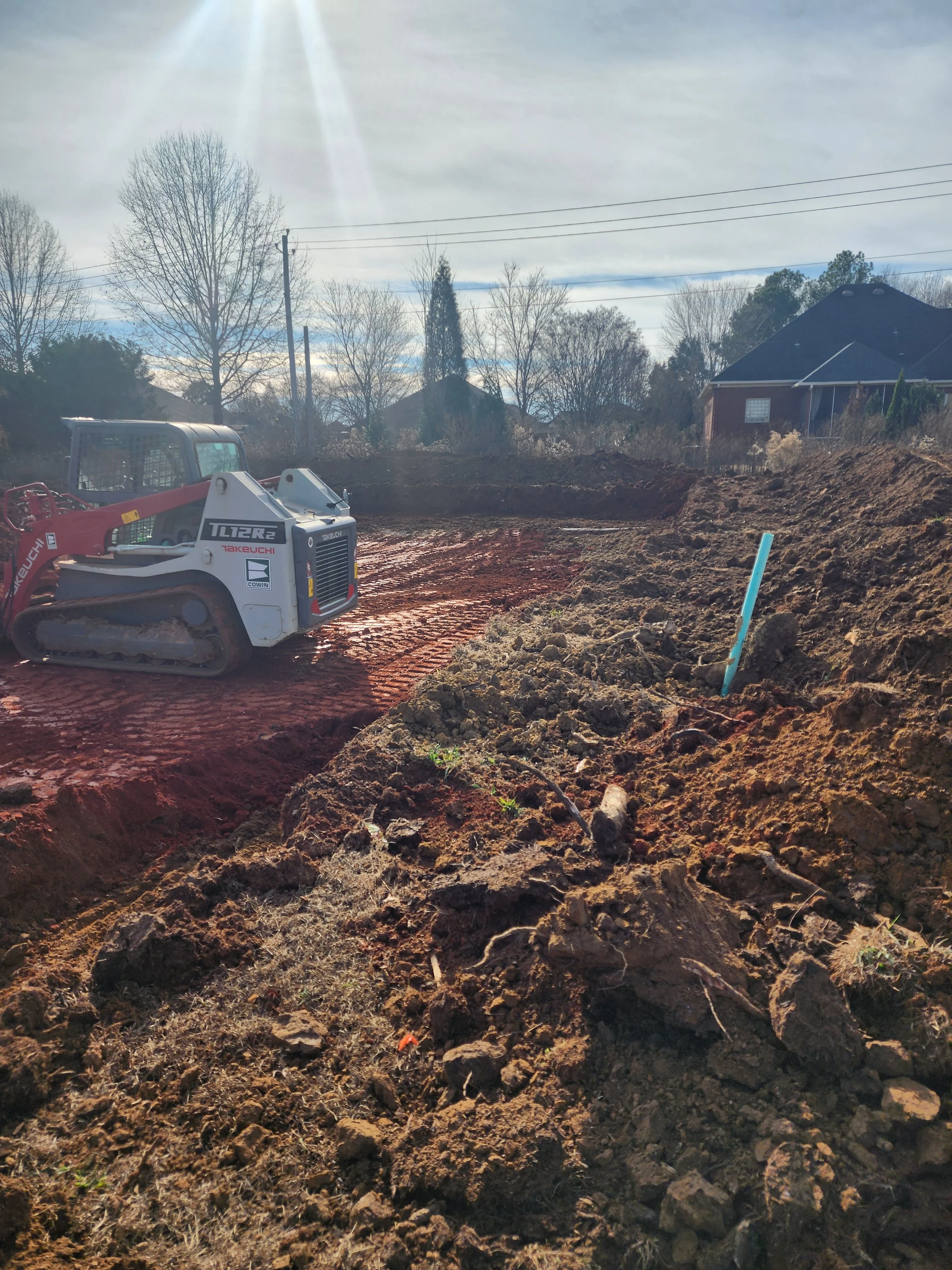 Bobcat track loader excavating and grading residential lot with piled soil